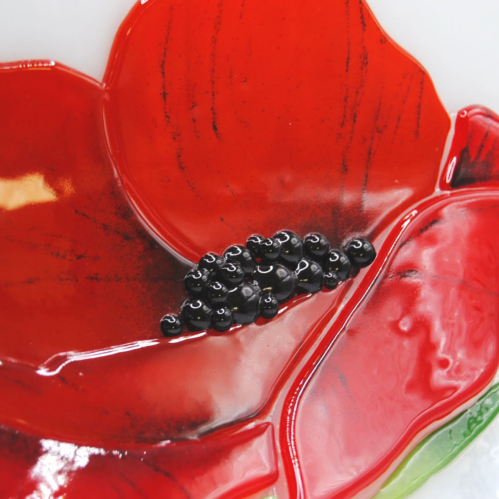 A close-up view of red glass petals with black glass beads attached, displayed on a wispy white glass plate.