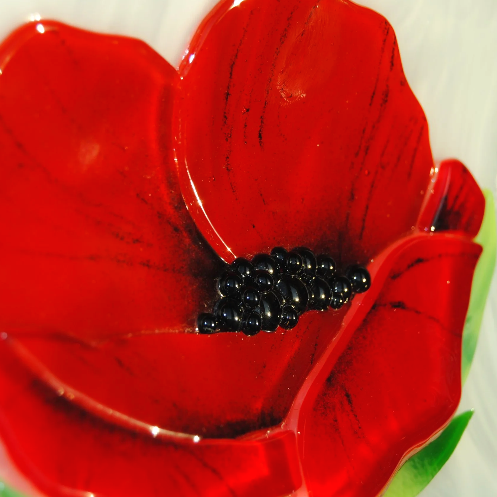 Close-up of a handcrafted red, flower-shaped glass bowl with black decorative beads at the center.
