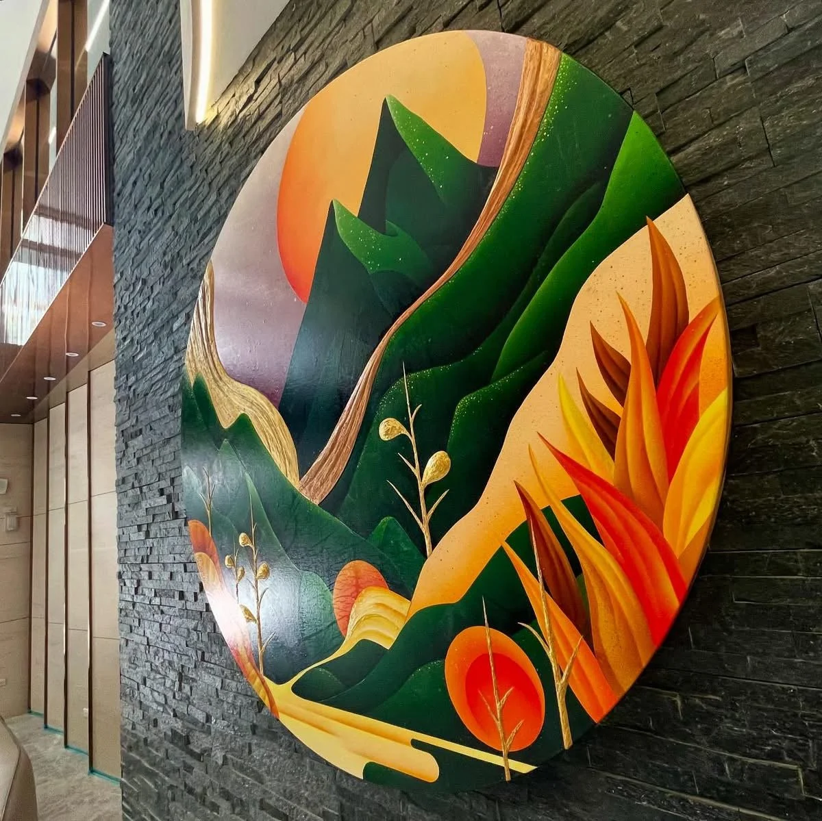 大型圓形藝術作品安裝於室內牆面，描繪層疊山巒、植被與暖色天空，呈現沉靜且具有延展感的自然意象