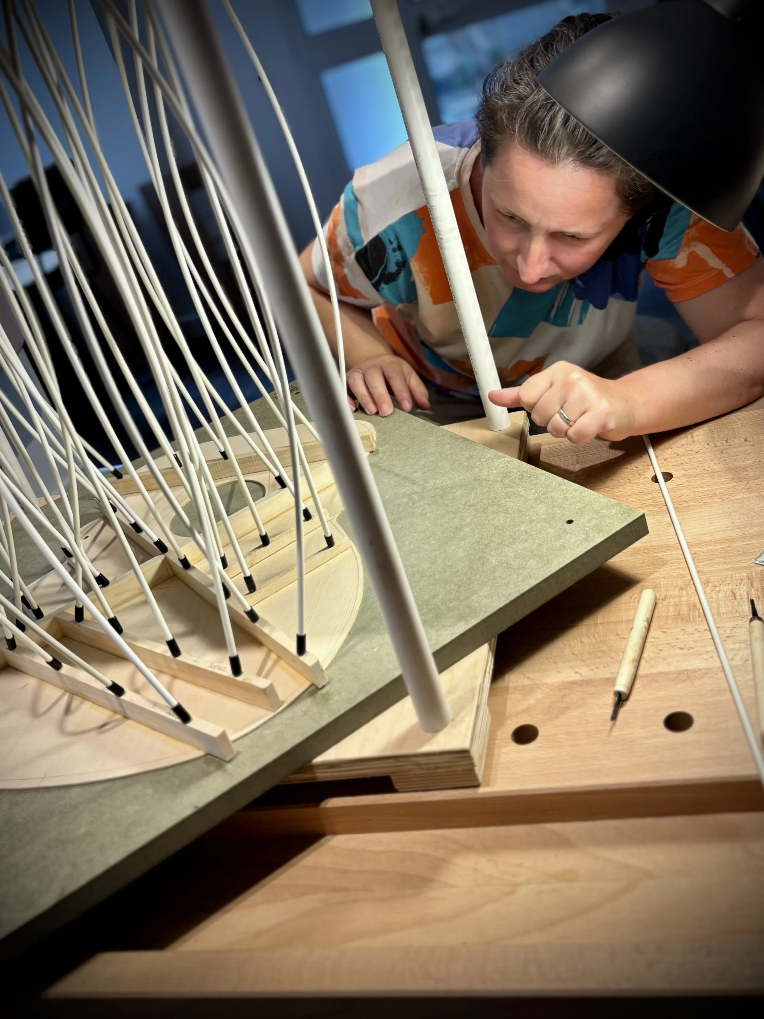 Donna che lavora su un modello di piroscafo in legno con alcune parti di tubo in plastica e strumenti da lavoro su un banco di lavoro.