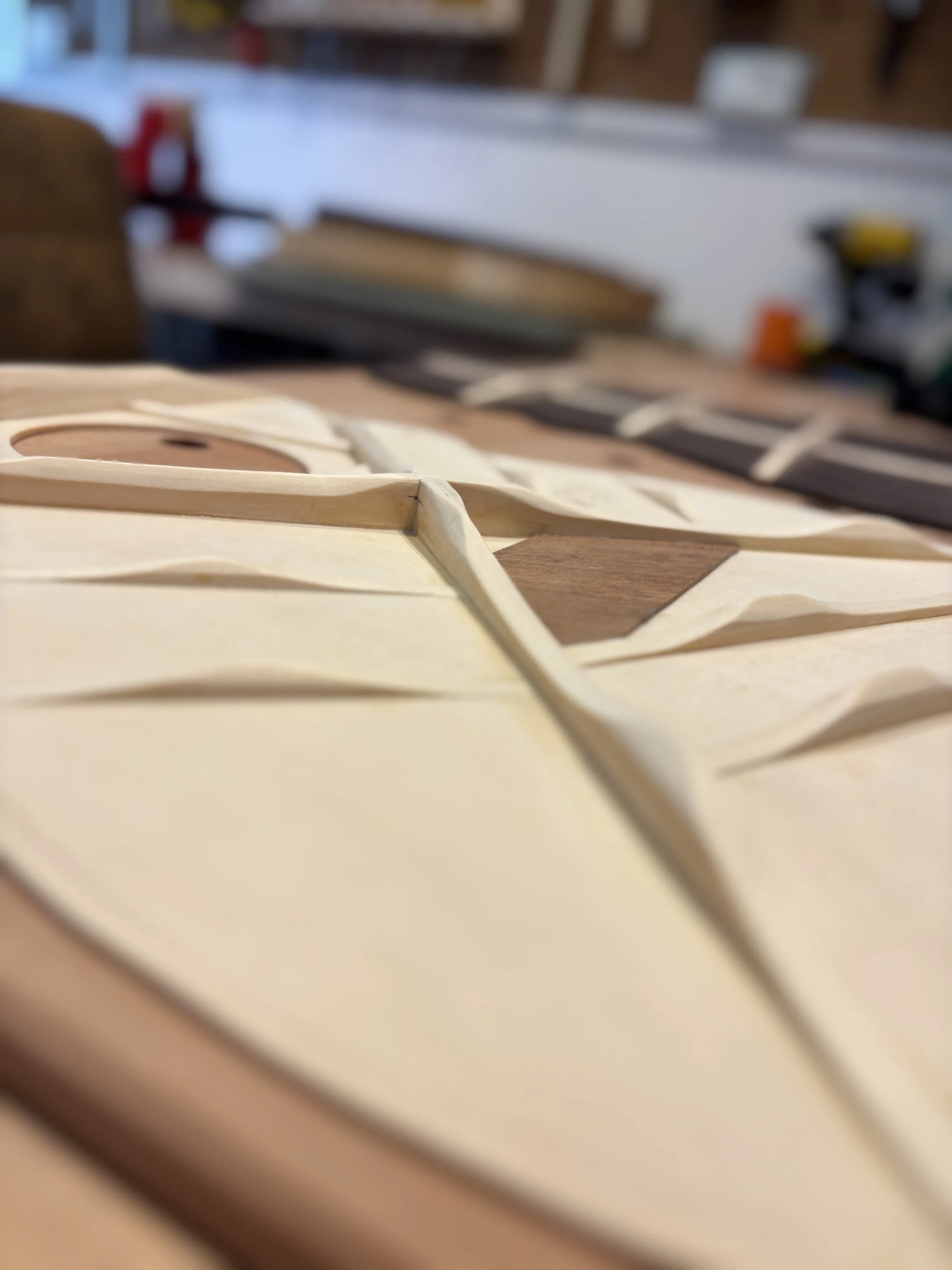 Parti di un modellino di aereo o veicolo in fase di assemblaggio su un tavolo di lavoro, con strumenti e altri pezzi visibili sullo sfondo.