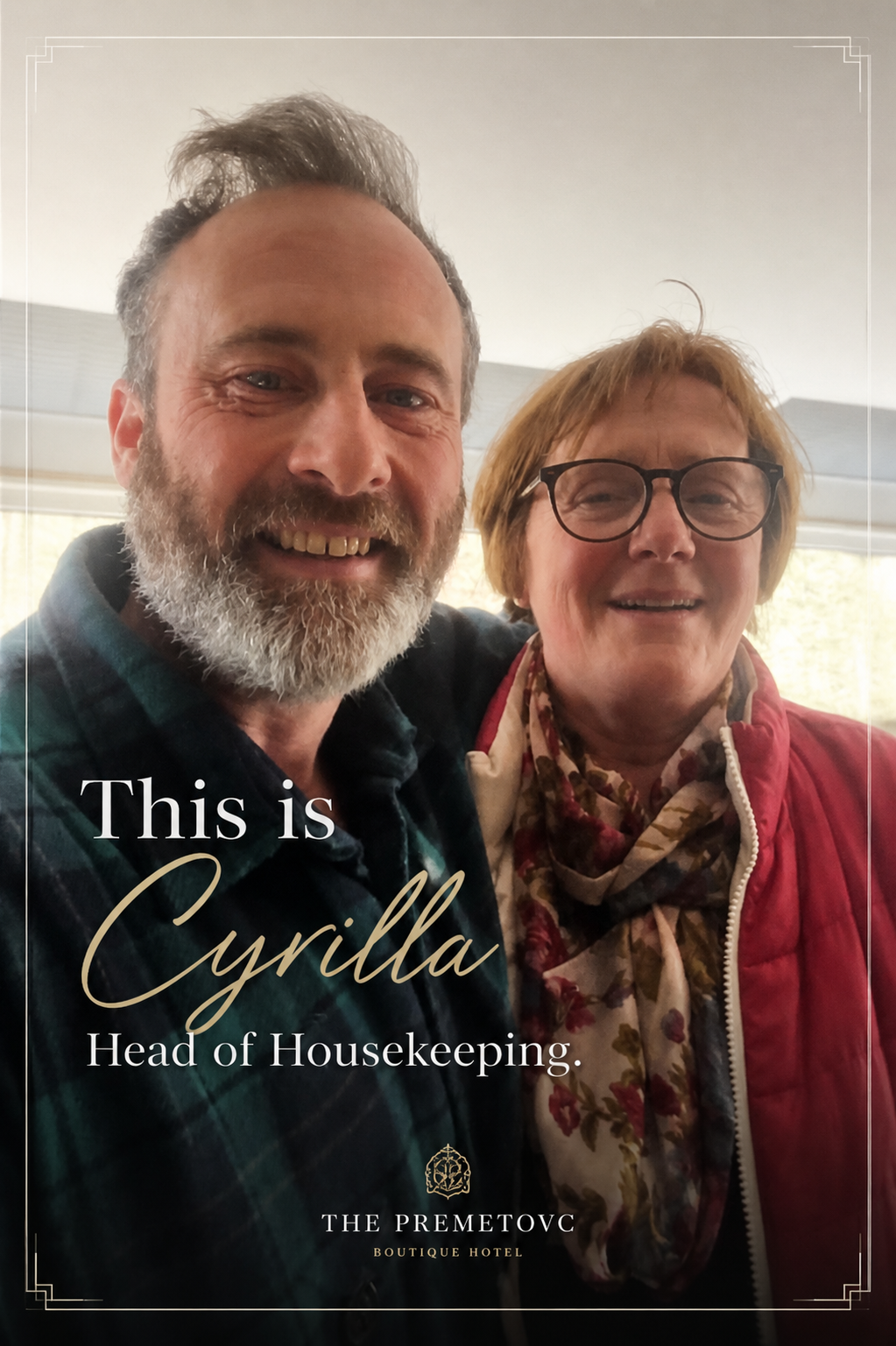 A man with a beard and a woman with glasses, smiling for a selfie, standing close together indoors near a window.