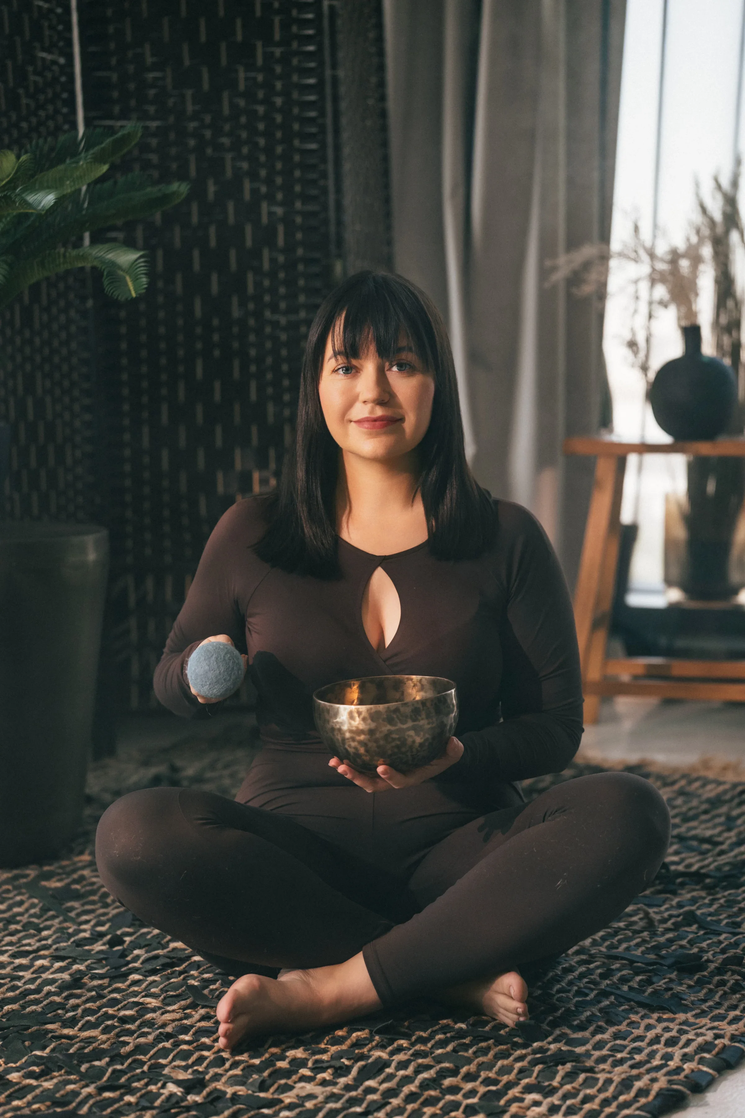 Vanessa Hartmann seated and looking at the camera while holding a Tibetan singing bowl during a trauma-informed sound healing session in Dubai.