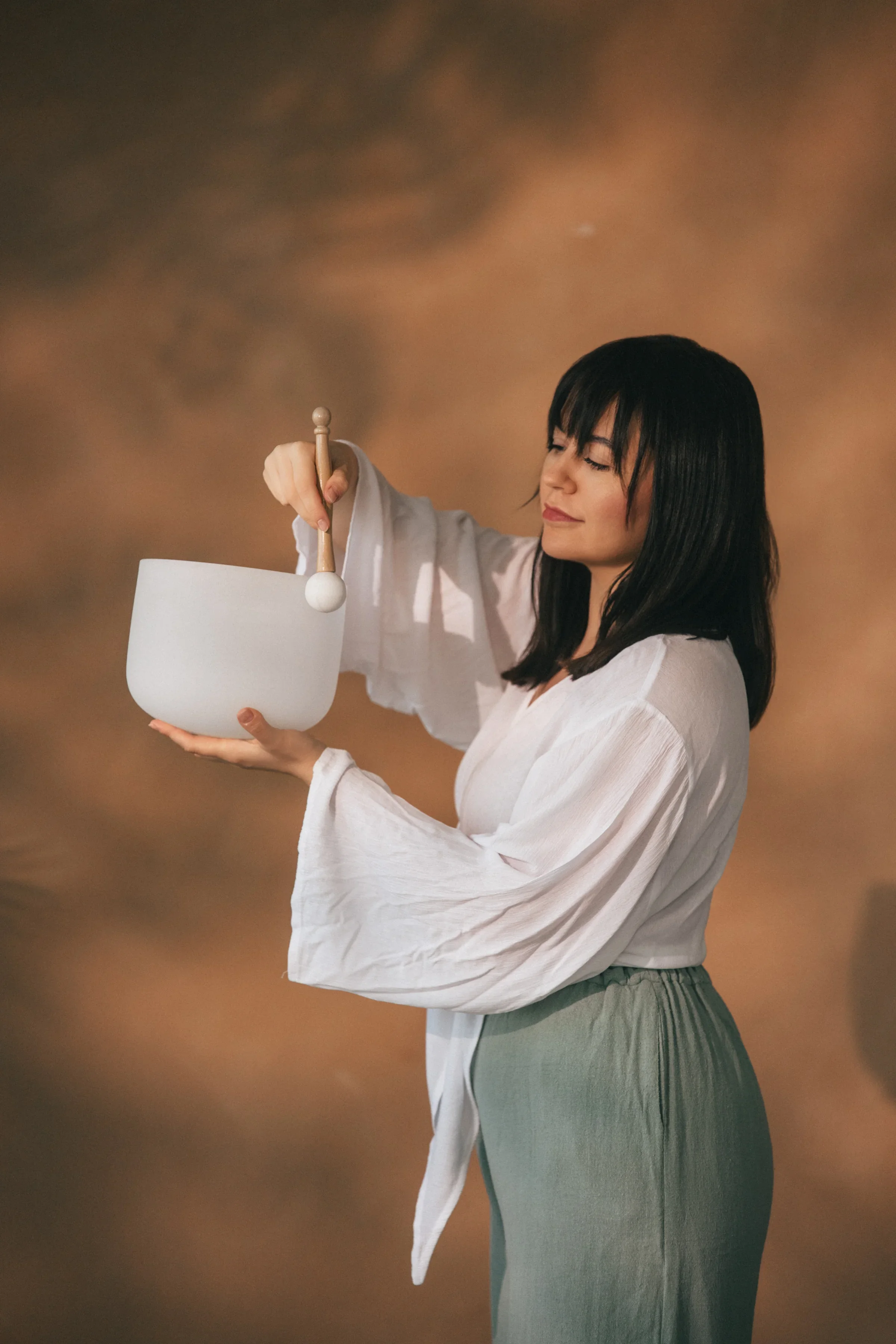 Vanessa Hartmann viewed from the side while holding and looking at a crystal singing bowl during a trauma-informed sound healing session for nervous system regulation in Dubai.