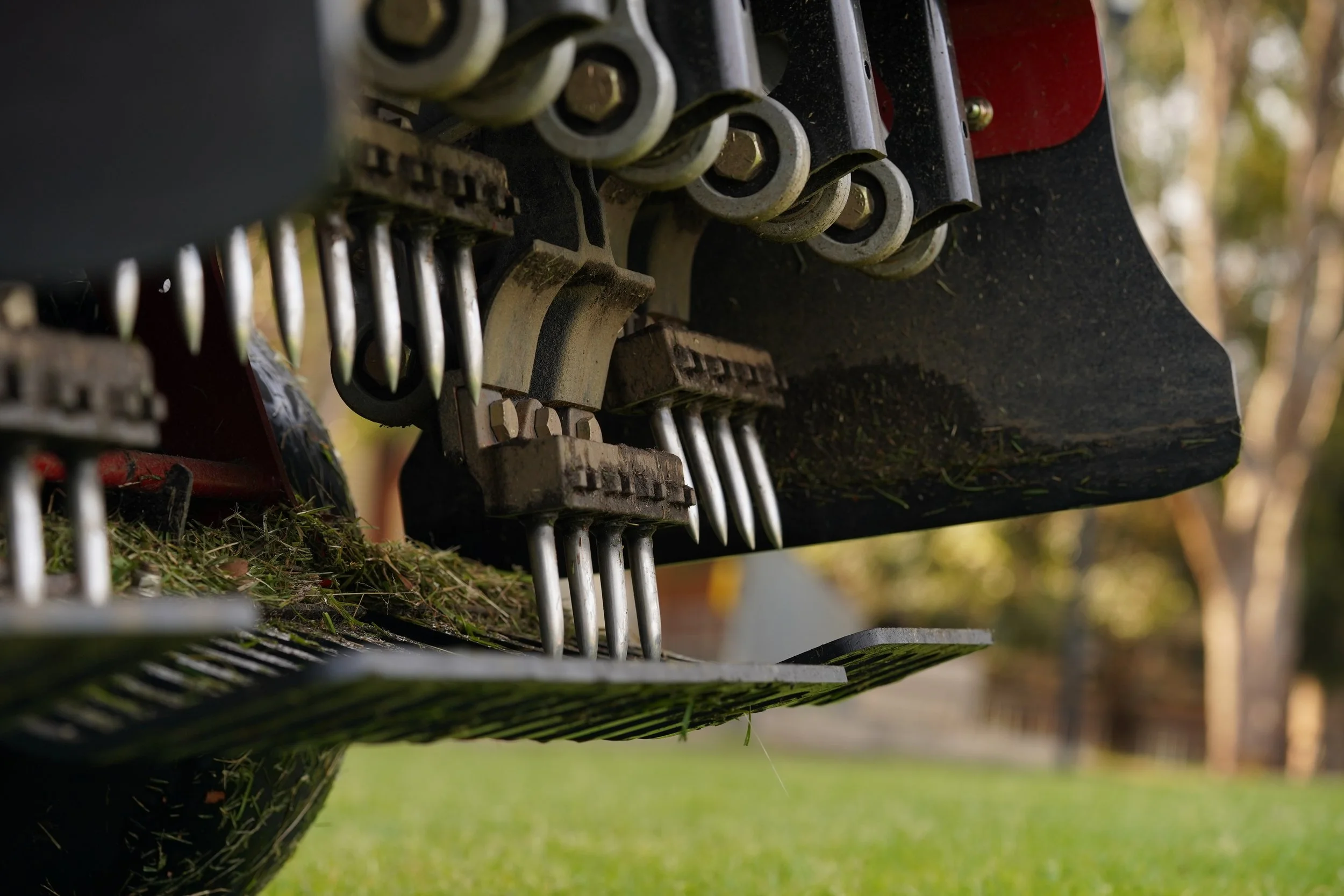 Close-up of a mechanical tractor part with gears, levers, and metal rods, outdoors on grass.