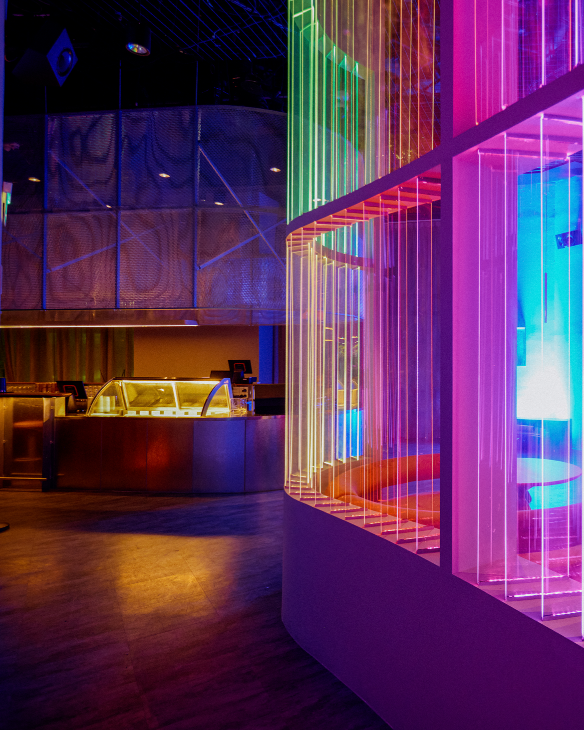 Interior of a nightclub with colorful neon lights, a curved glass display counter, and metallic surfaces.