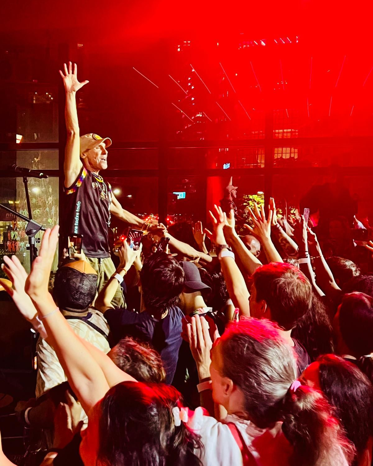 A person on stage in front of a crowd, reaching out, with people raising their hands and taking photos at night.