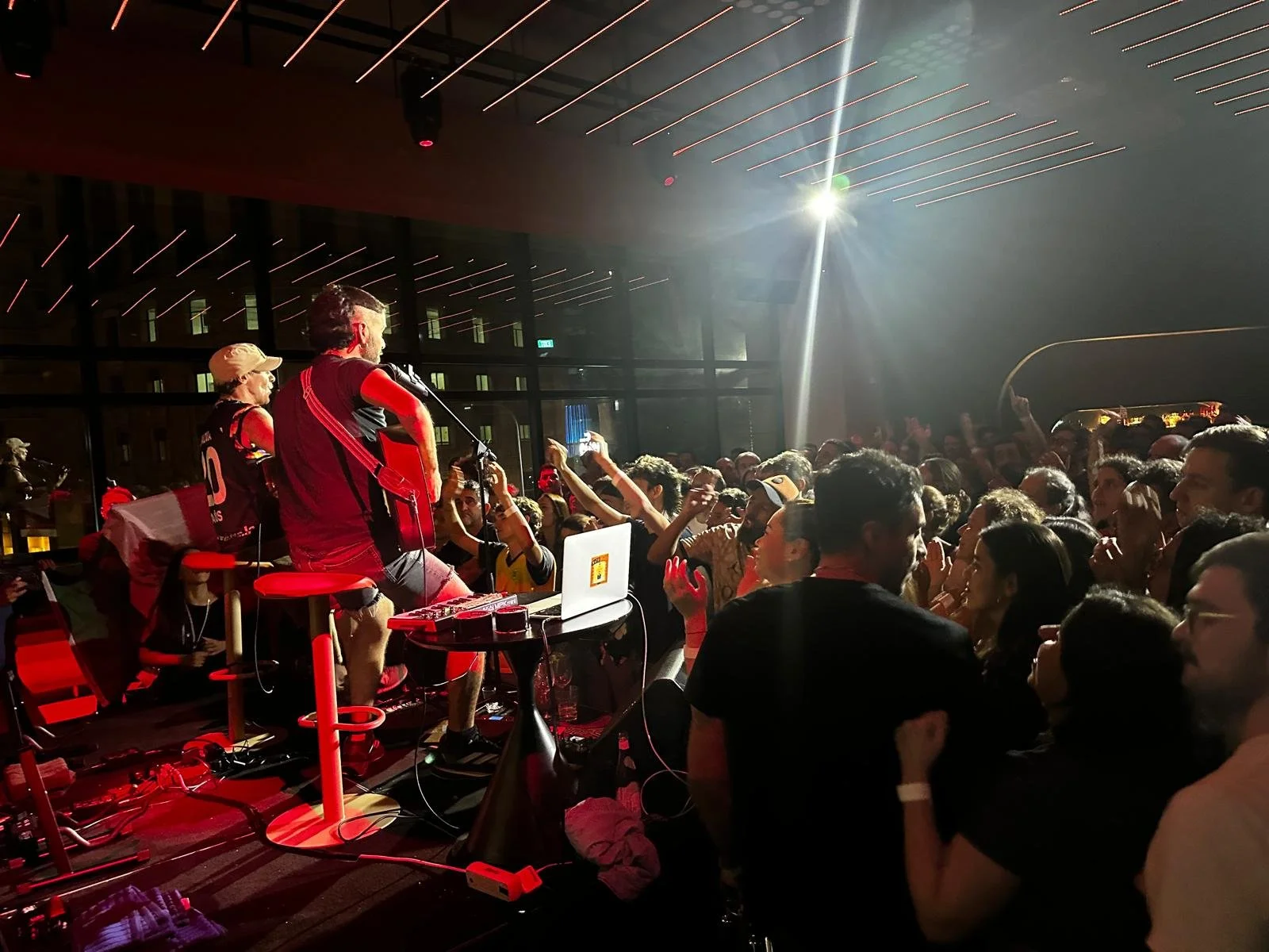 Musicians performing on stage with a crowd dancing and enjoying the music in front of them. Bright stage lights and a modern venue are visible.