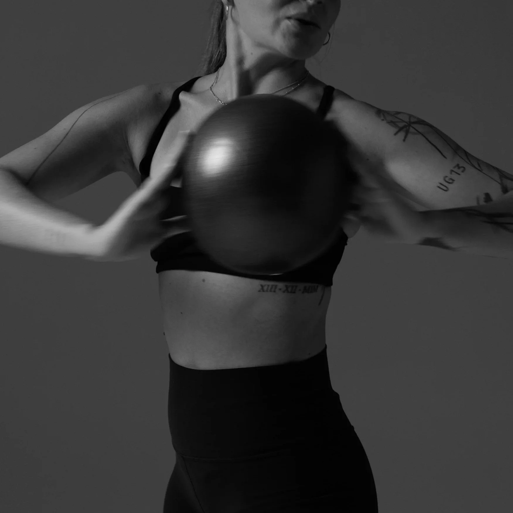 A woman in workout attire holding a kettlebell, with tattoos visible on her arm, in a gym setting.