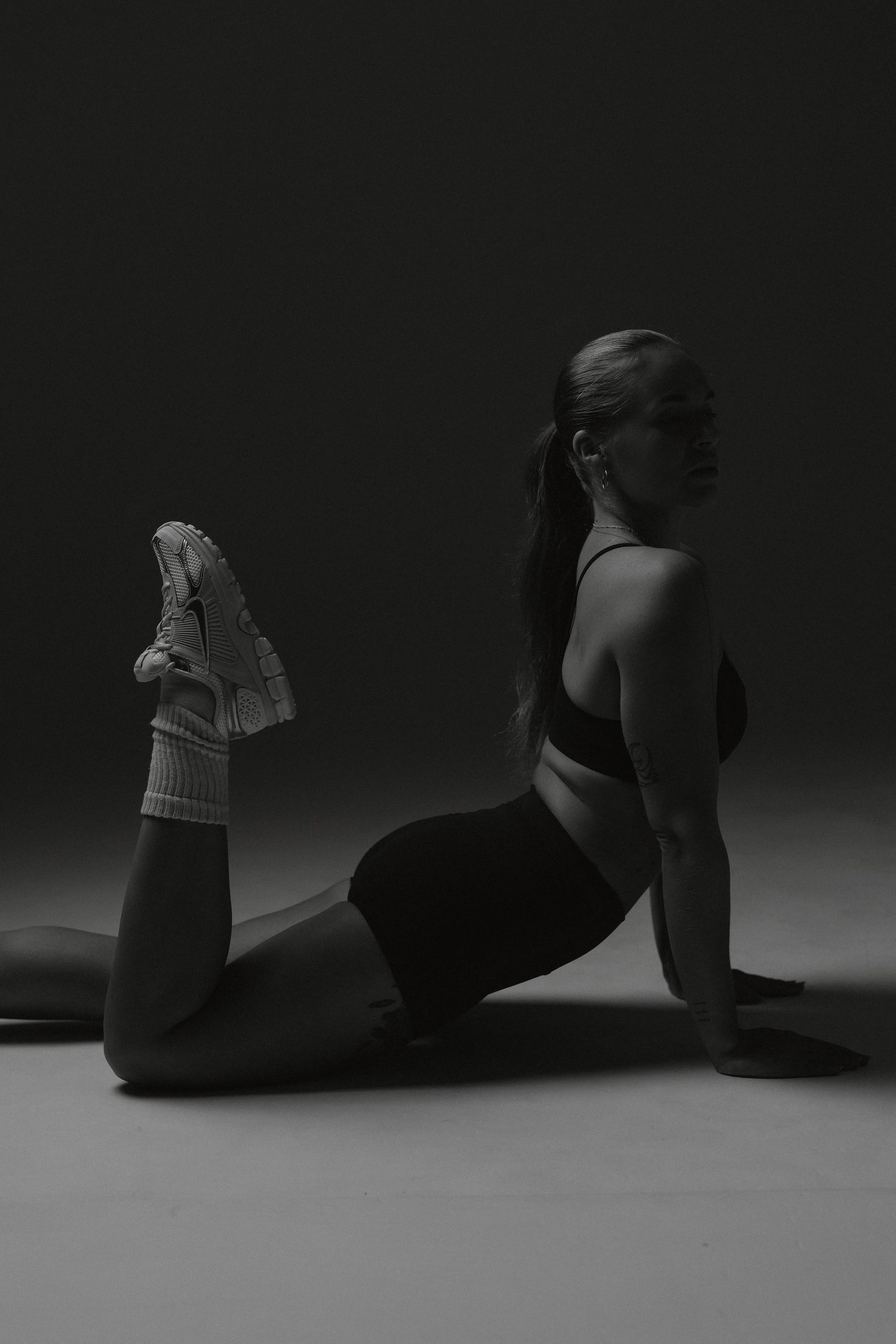A woman in athletic clothing performing a yoga pose on a plain surface with a gradient dark background.