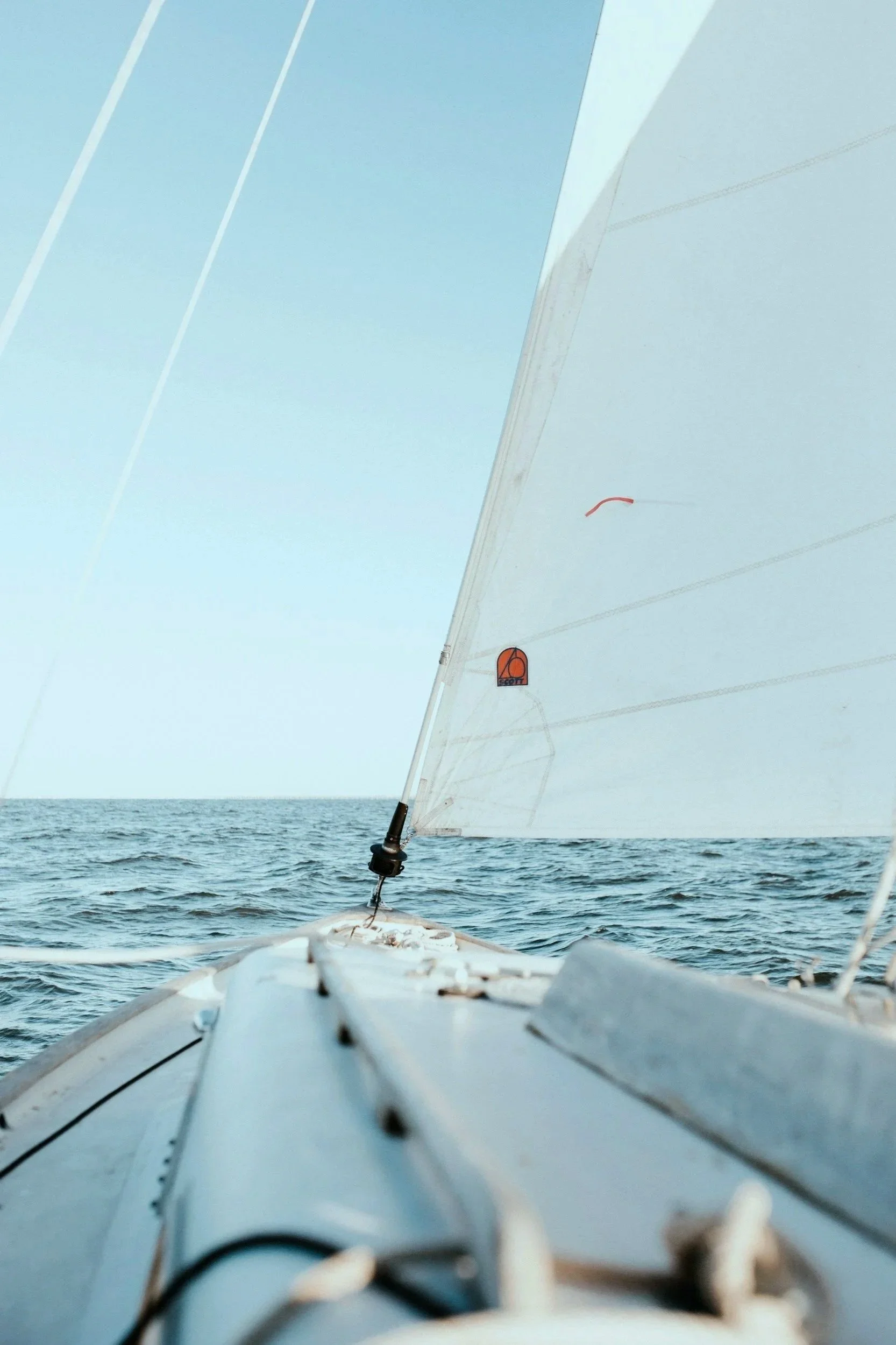 Vue depuis un bateau à voile sur la mer avec une voile blanche et un fond de ciel clair.