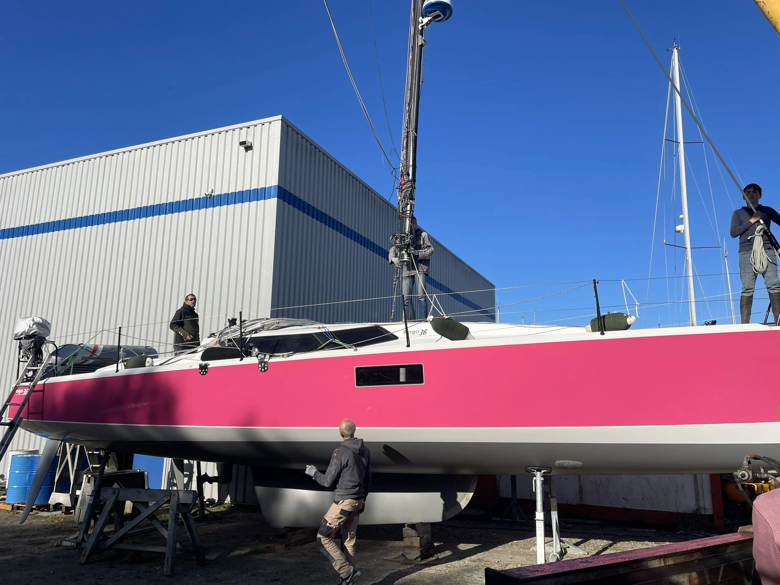 Un yacht rose en construction dans un chantier naval avec des ouvriers travaillant dessus, sous un ciel dégagé.