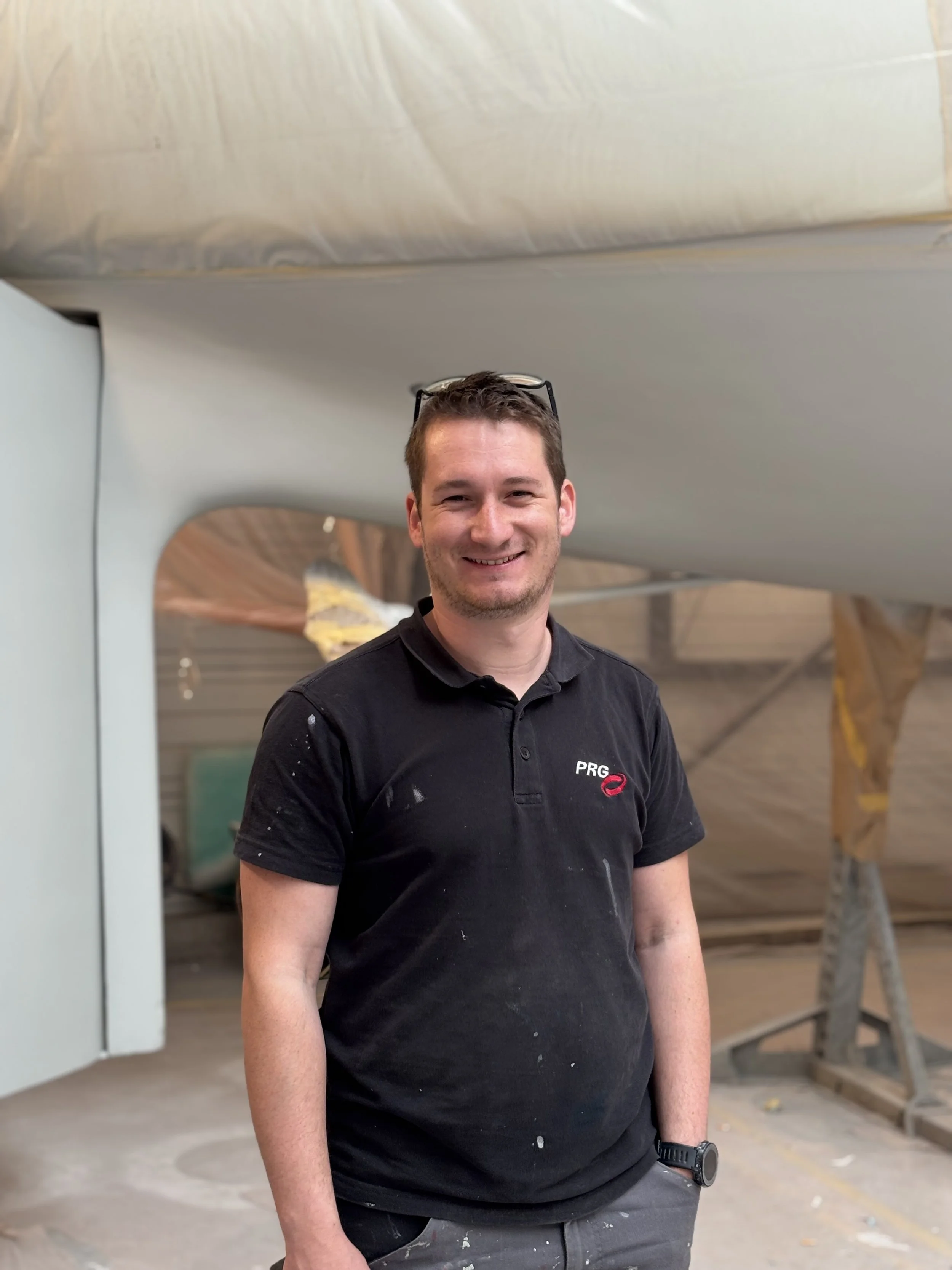 Un homme souriant portant une chemise noire avec le logo 'PRG' devant une structure en bois dans un environnement intérieur.