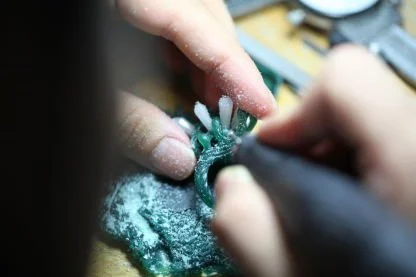 A person is using tools for wax carving, with dust and debris scattered around.