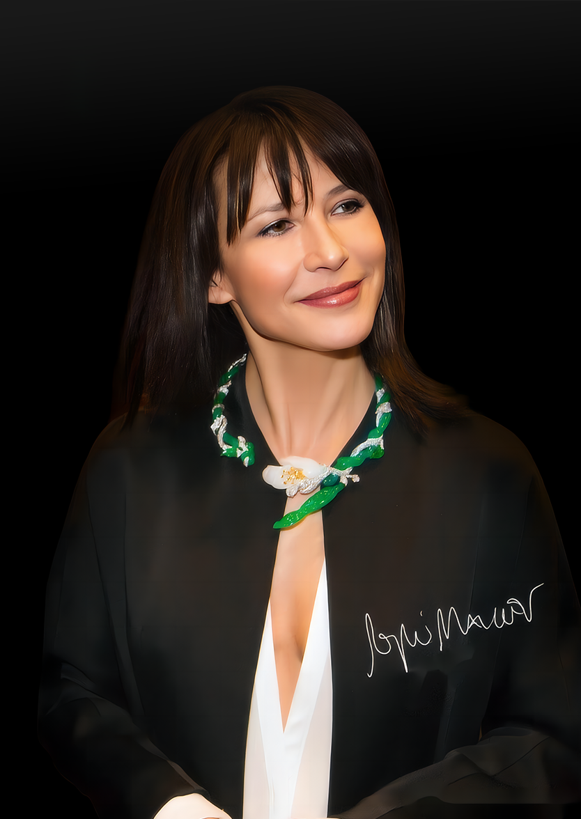 A woman with brown hair and a gentle smile, wearing a black jacket with an autograph on it, and a colorful beaded necklace against a black background.