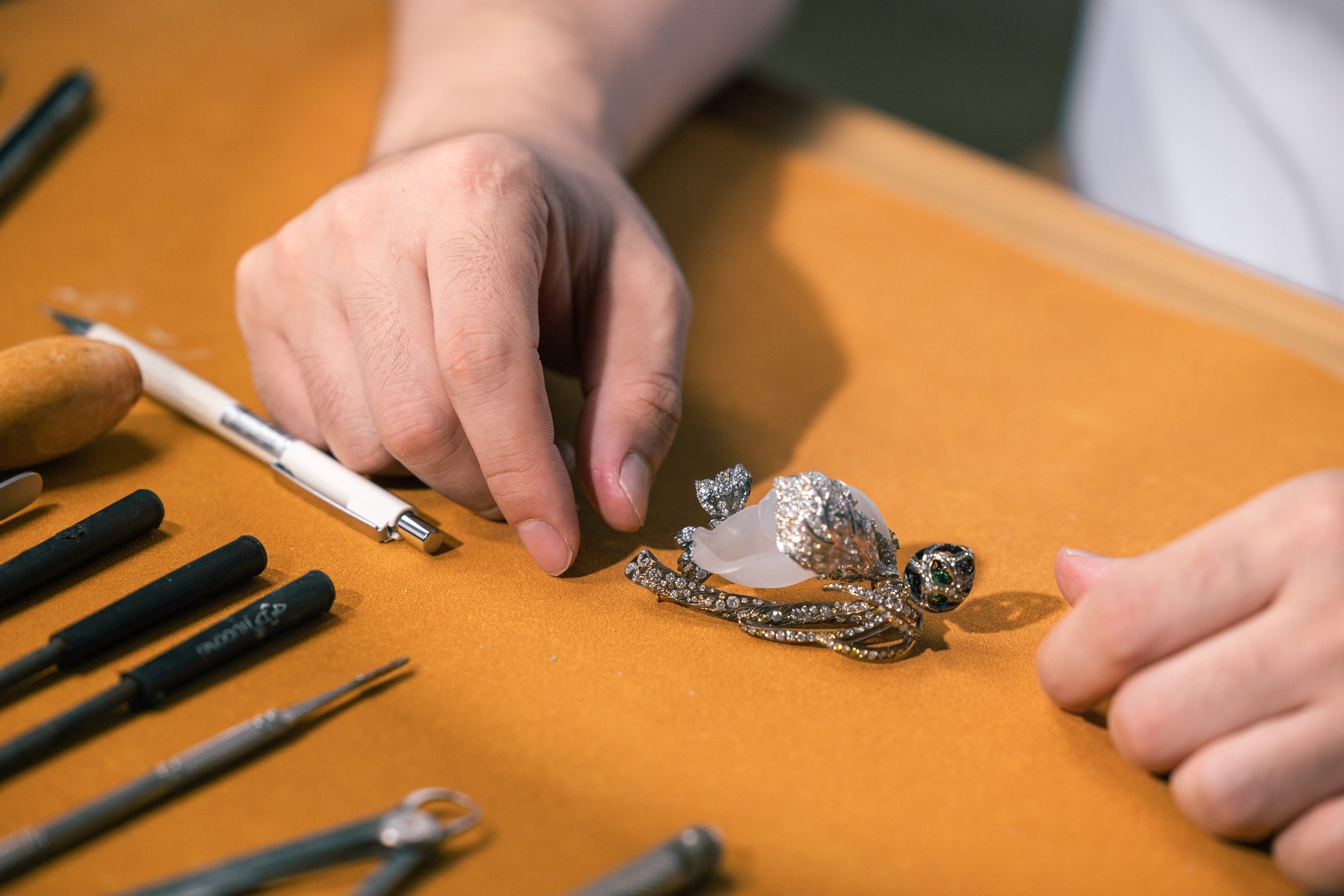 Person's hands working on a jewelry piece at a workbench with tools.