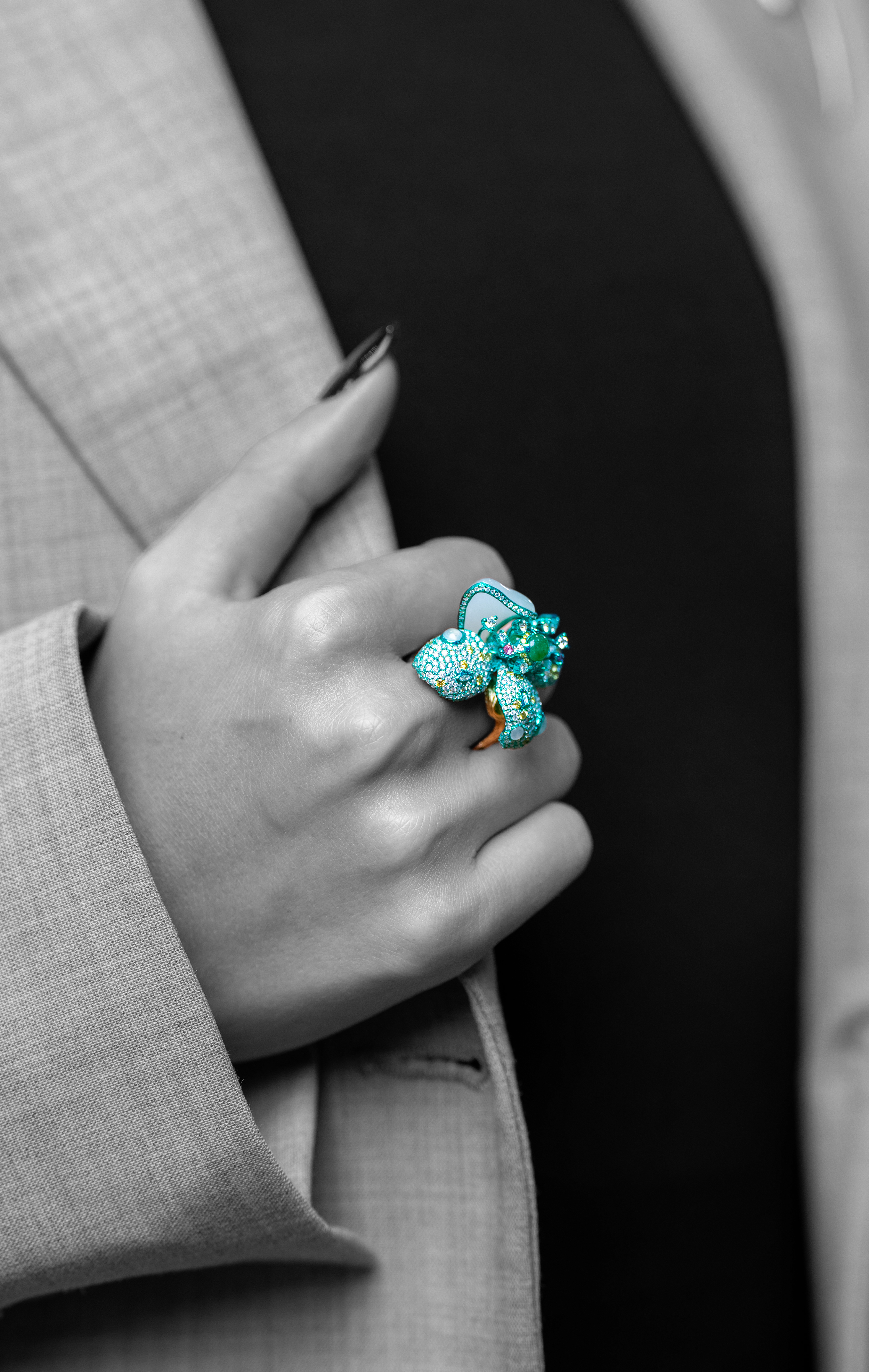 In a close-up shot, a hand wears a Hetian jade and diamond butterfly ring. The rest of the image is in black and white, showing a person in a suit jacket in the process of wearing it.