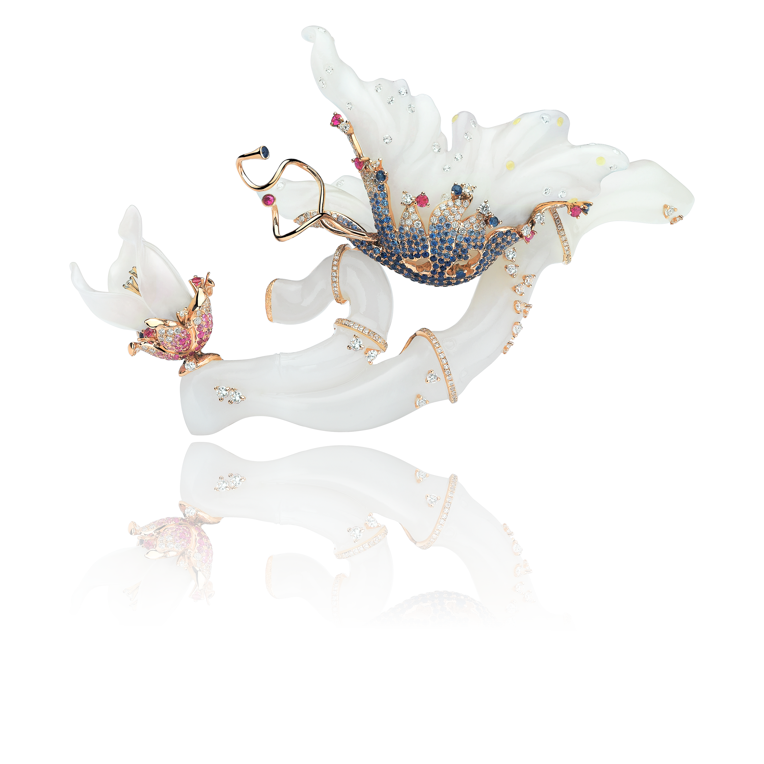 Jewelry brooches in the shape of butterflies and a flower, adorned with pink, blue, and clear gemstones, placed on a white jade or jade branch.