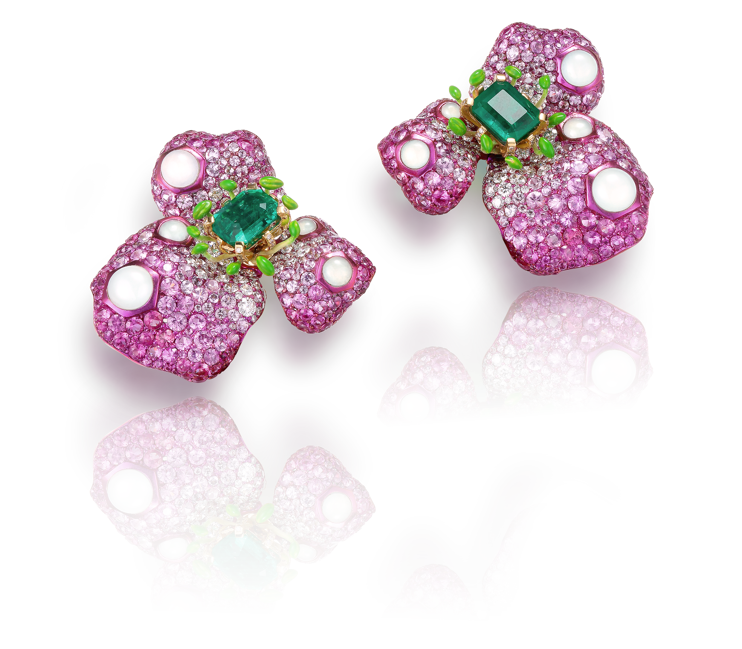 Pink floral earrings encrusted with pink and white stones, with a central green gemstone, on a reflective black surface.