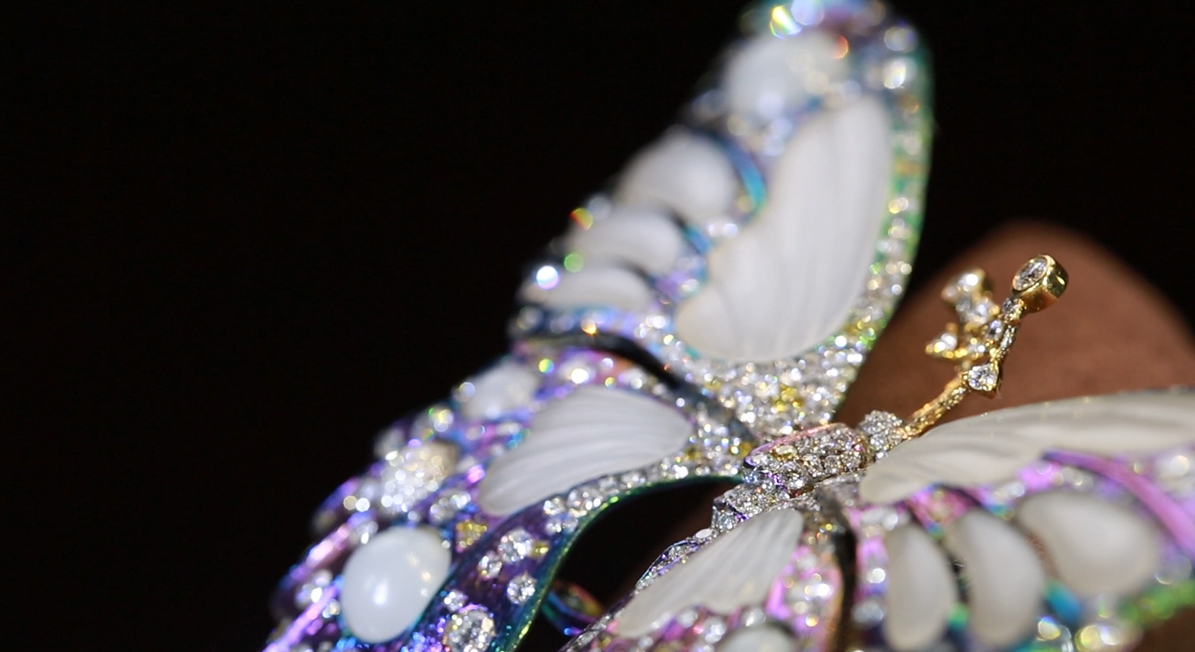Close-up of an ornate, jeweled butterfly brooch with white wings and colorful rhinestones against a black background.
