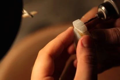 A hand holds carving tools, working on a piece of jade.
