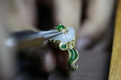 During the jewelry-making process, pliers are used to handle a ring set with Hetian jadeite, gold accents, and white Hetian jade.