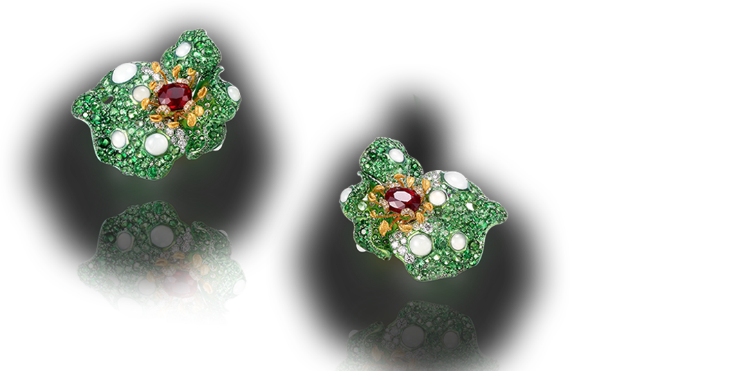 Pair of emerald and diamond earrings with a central red gemstone set on a reflective black surface.