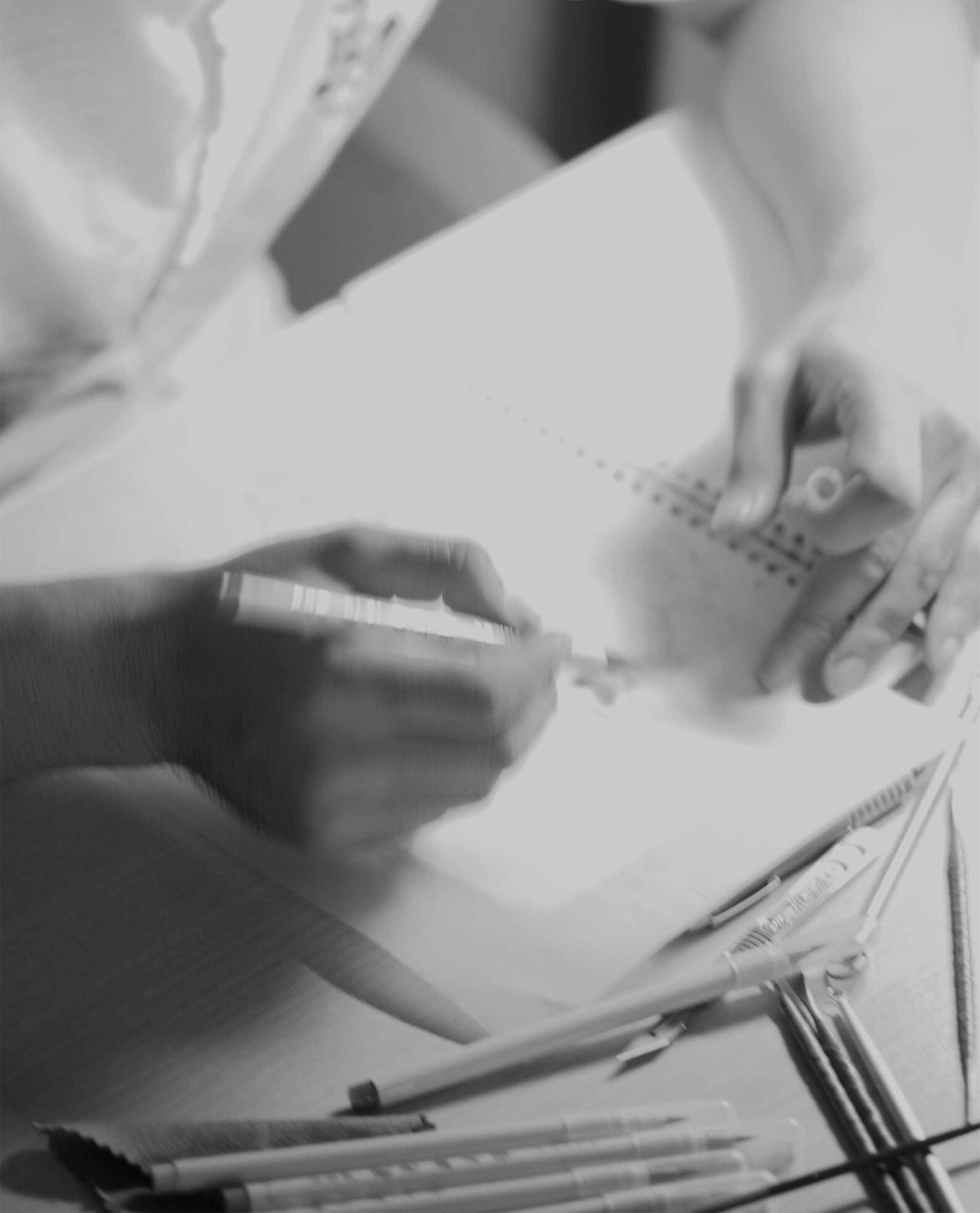 Close-up of a person's hands sketching on a blank sheet of paper, with various pens and markers scattered on the table.
