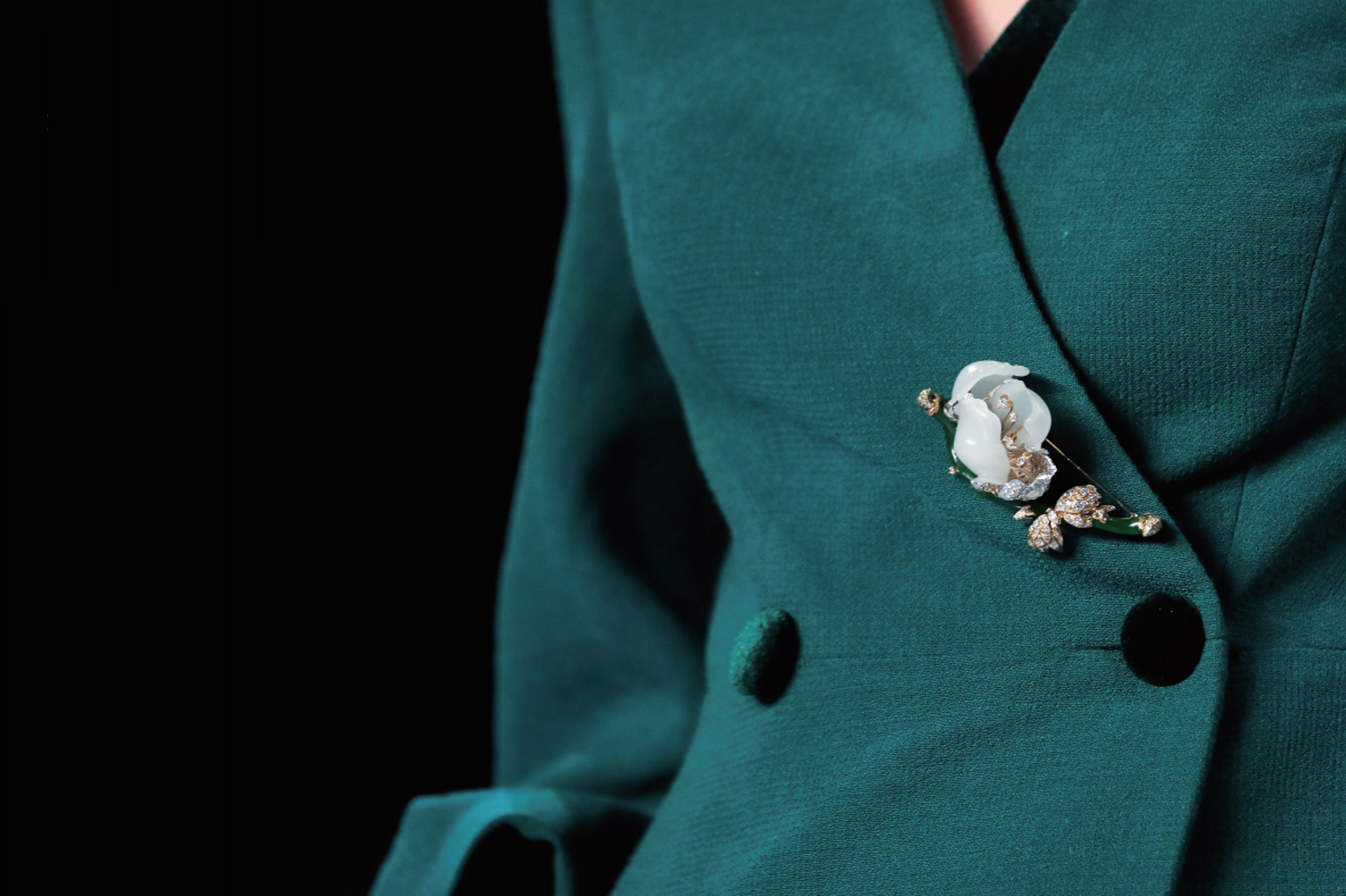 Close-up of a teal blazer with a decorative brooch featuring white flowers and gold accents.