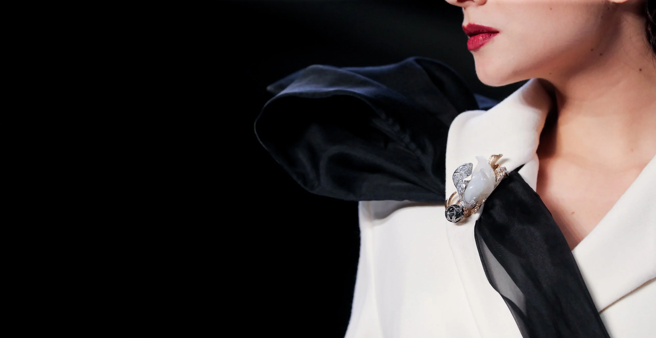 Close-up of a woman wearing a white outfit with a black sheer scarf and a decorative brooch on her shoulder.