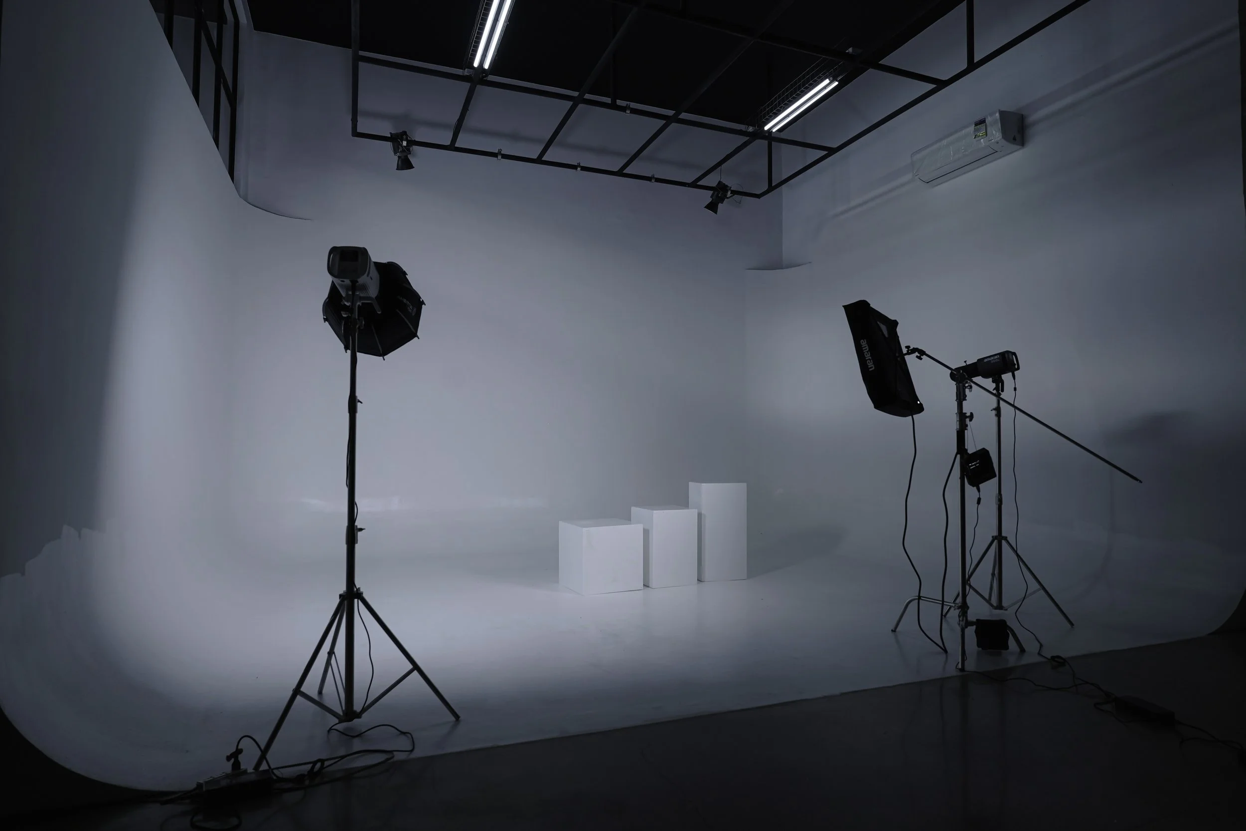 A photography studio with a white backdrop, professional lighting equipment, and three white podiums arranged in a row.