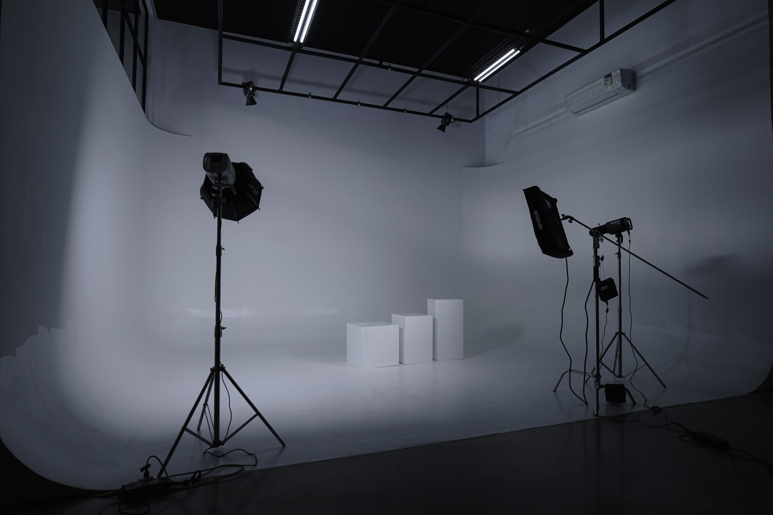 Photography studio with lighting equipment and white background, three white podiums of different heights in the center.