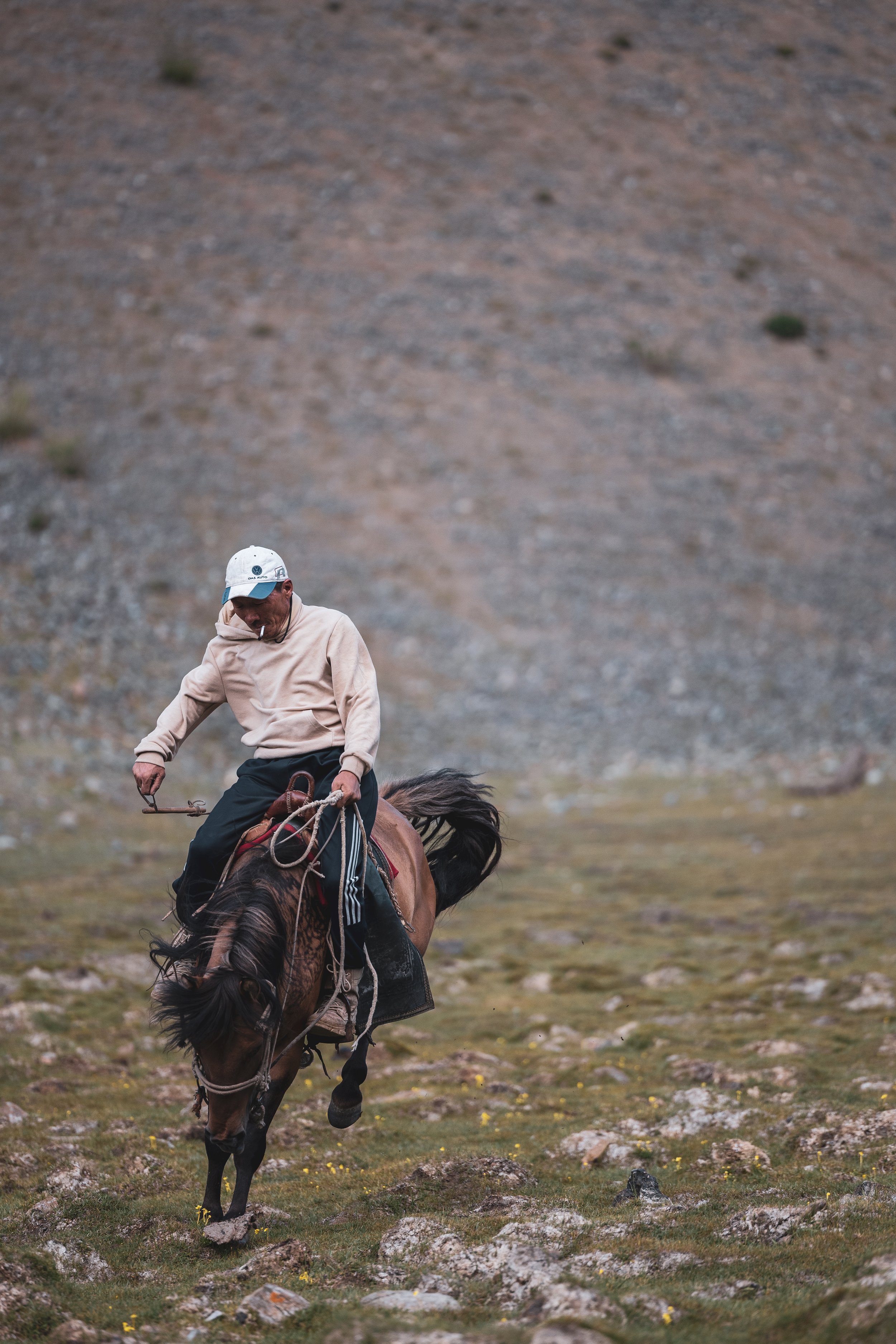 Man riding a brown horse across a rocky and grassy landscape with a mountain in the background.