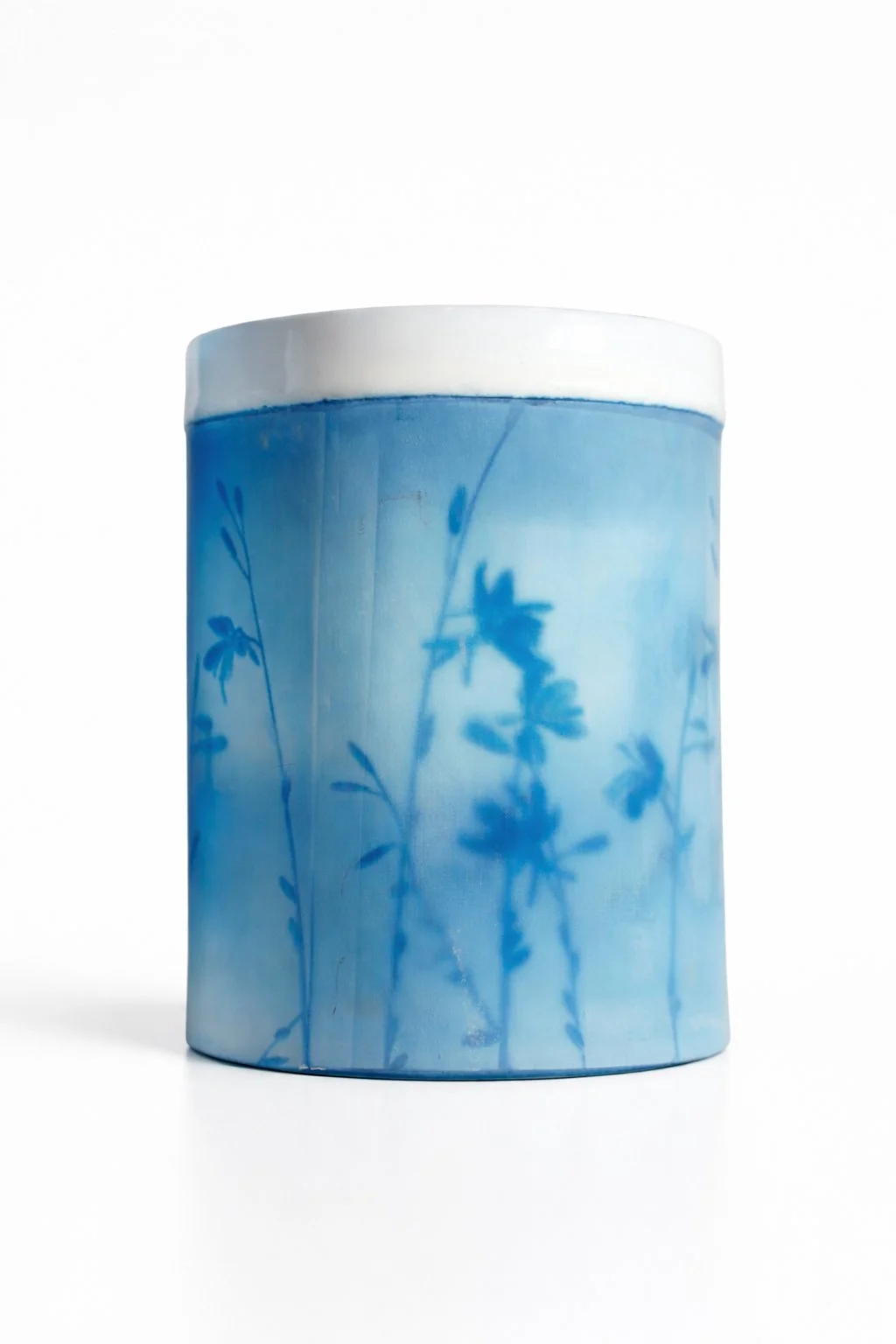 Une boîte cylindrique en céramique ou en porcelaine avec un motif décoratif de fleurs bleues sur un fond dégradé du bleu clair au bleu foncé.