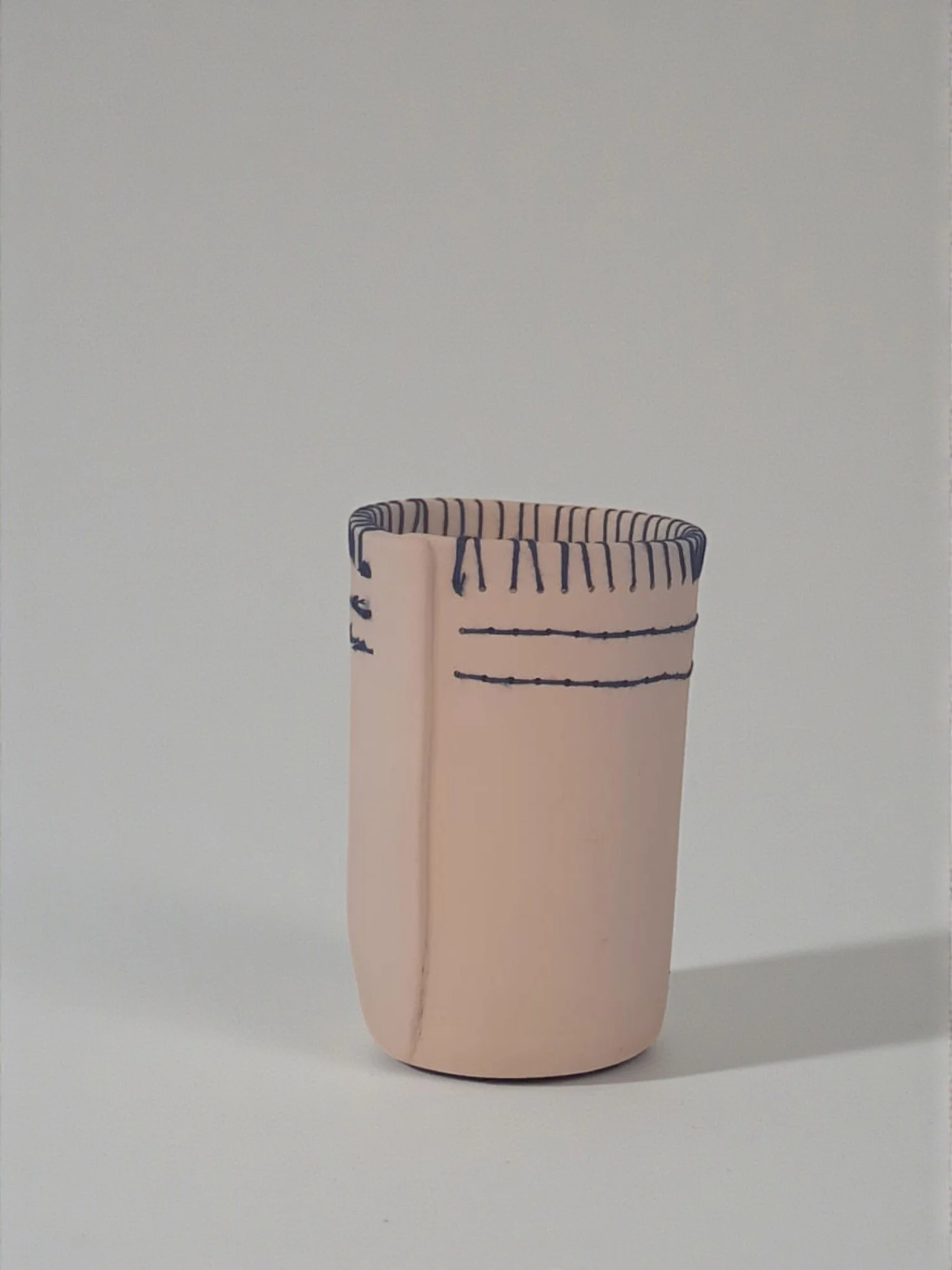 Vase en céramique de couleur rose avec des lignes bleues, posé sur un fond blanc.