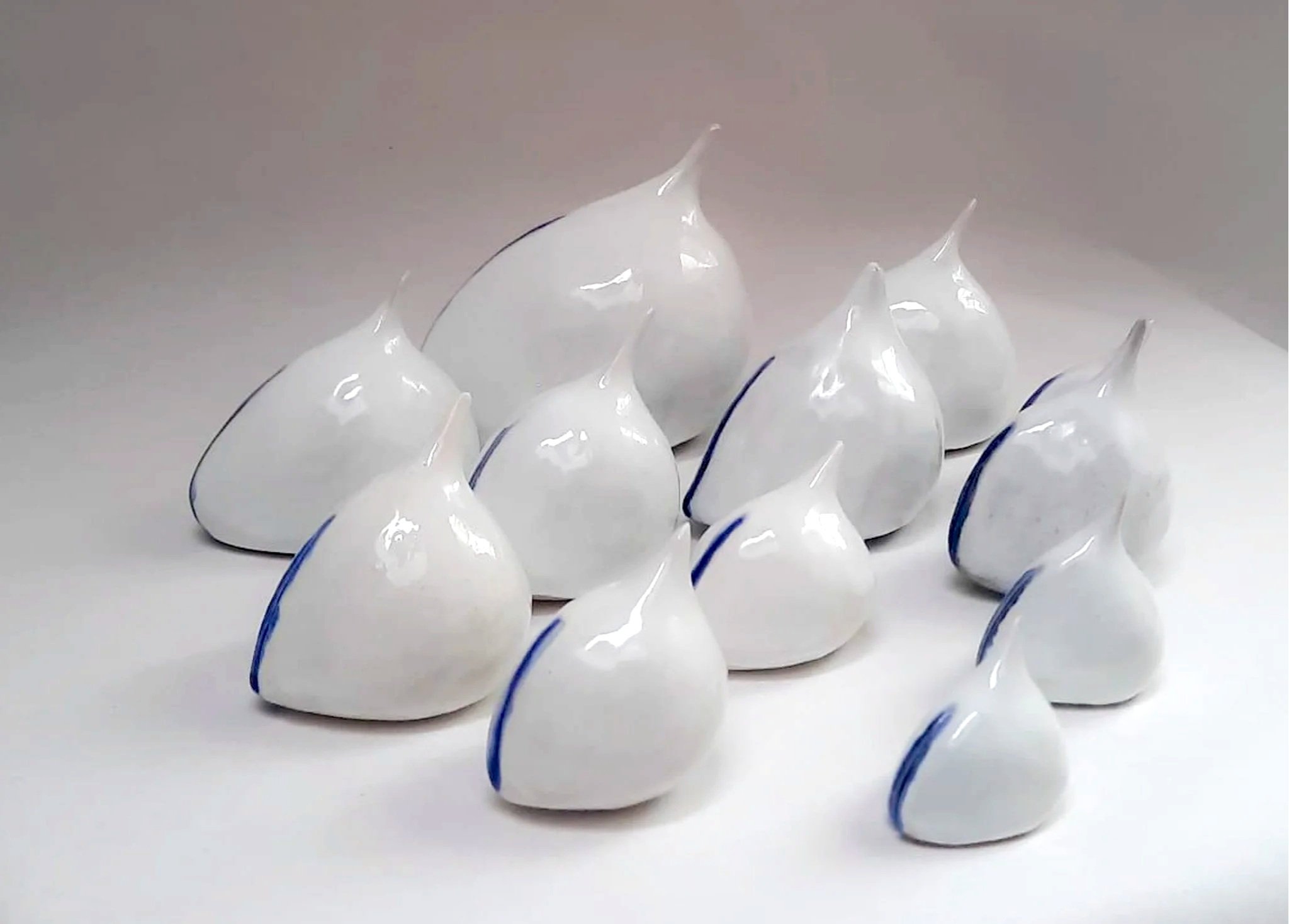 Groupe de sculptures en verre blanc en forme de goutte, avec des lignes bleues, sur un fond blanc.
