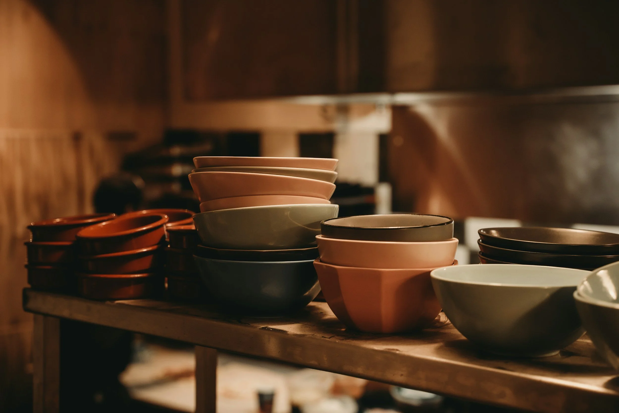 Stacked ceramic bowls on a wooden table in a dimly lit rustic kitchen.