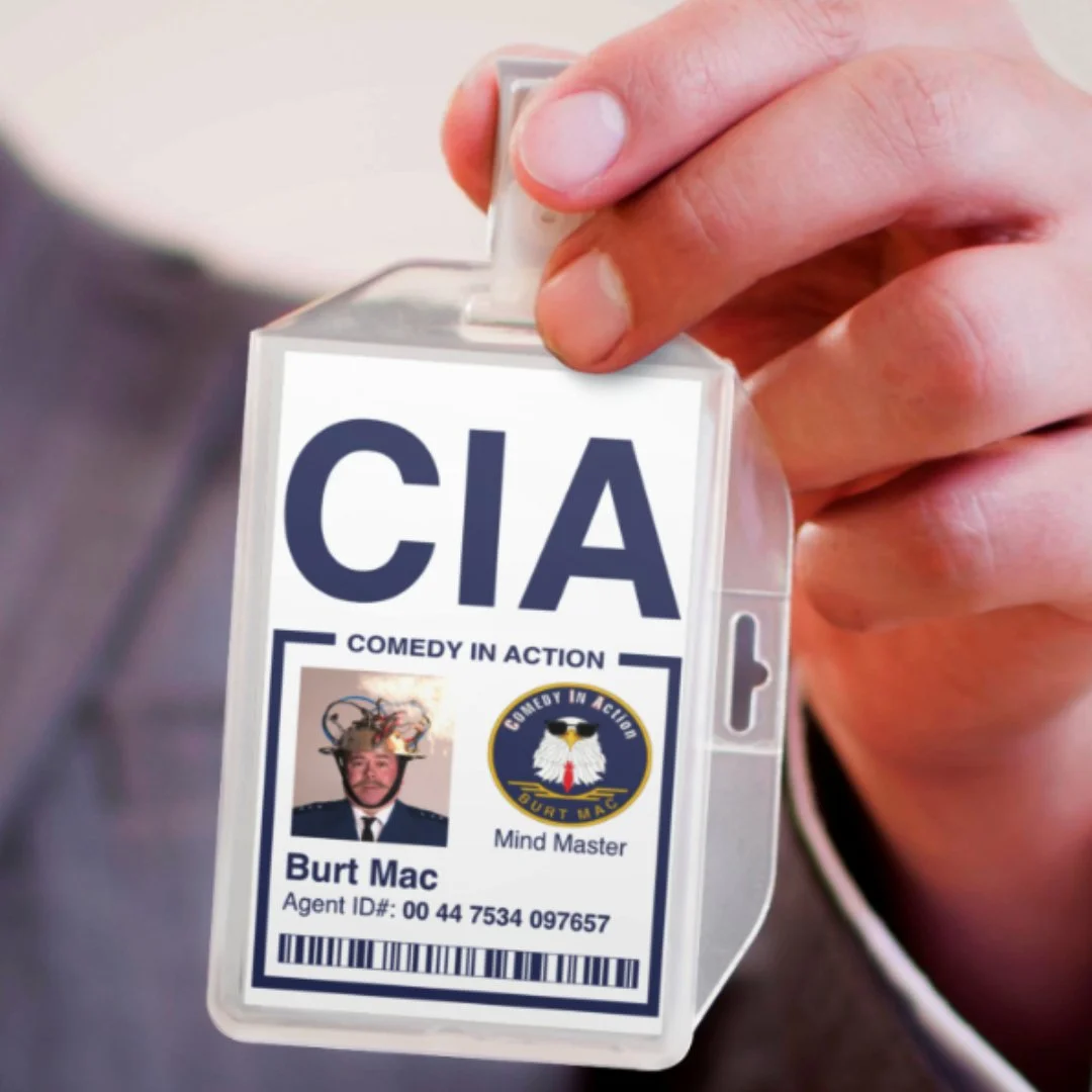 A person holding a CIA badge with a humorous picture of a man with an elaborate headpiece, the CIA logo, and the text "Comedy in Action" and "Mind Master."