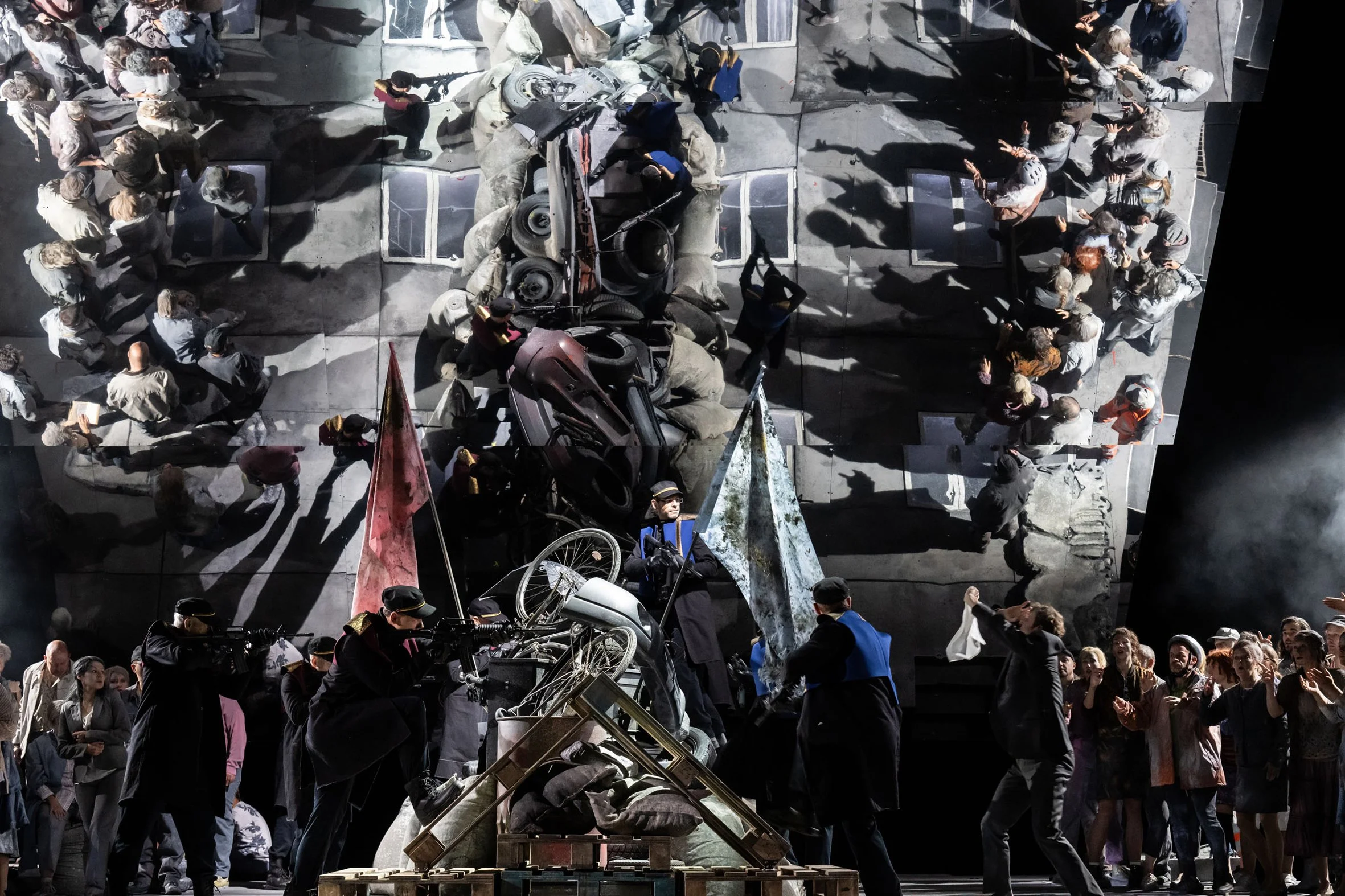 Szenisches Theater mit Menschen, Requisiten und Kulissen, die einen Krieg oder Konflikt darstellen, inklusive zerbrochener Autos und Rauch.