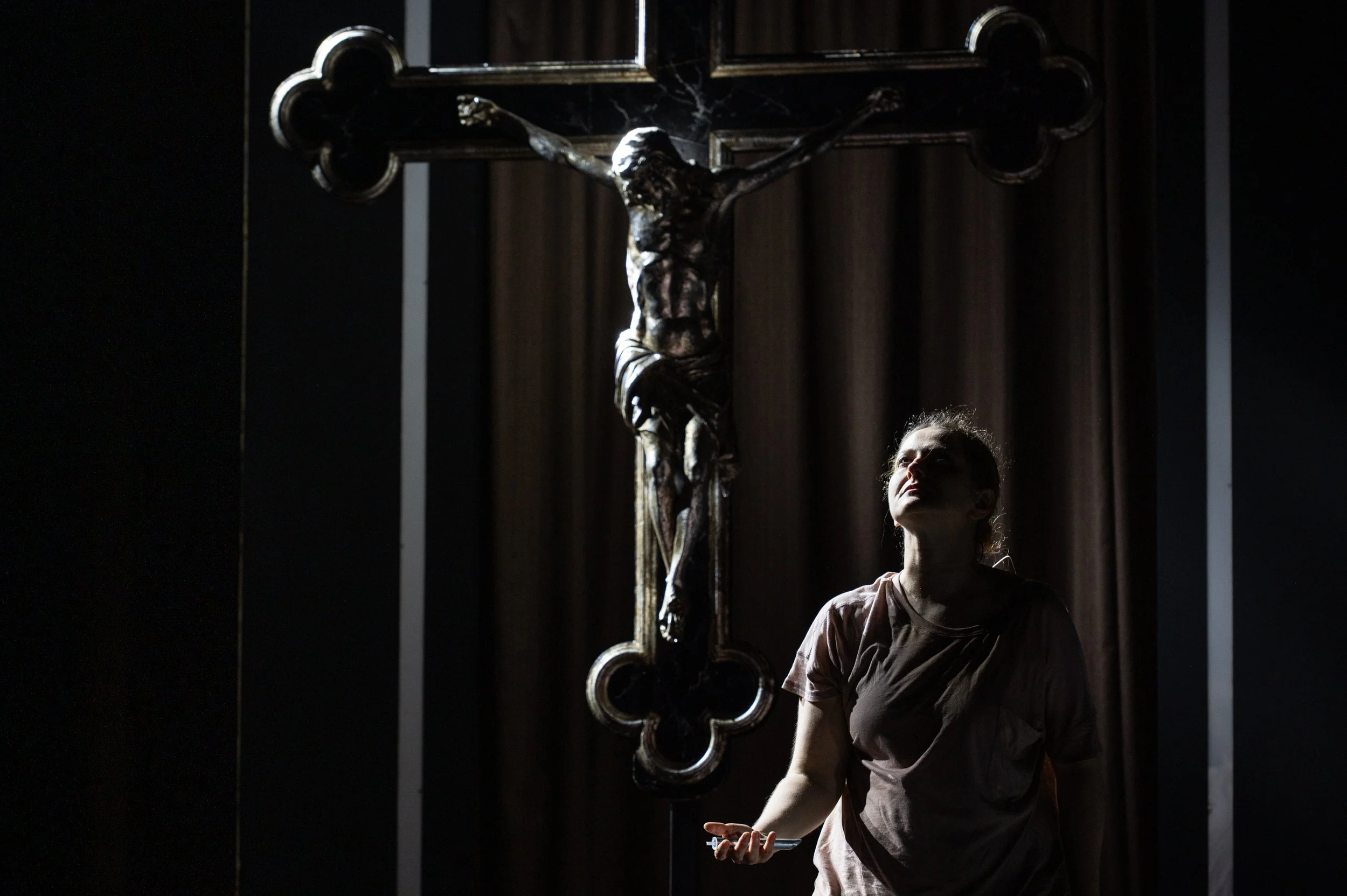 Ein junges Mädchen steht vor einem großen Kreuz mit einer Skulptur von Jesus Christus, das von Licht hervorgehoben wird.