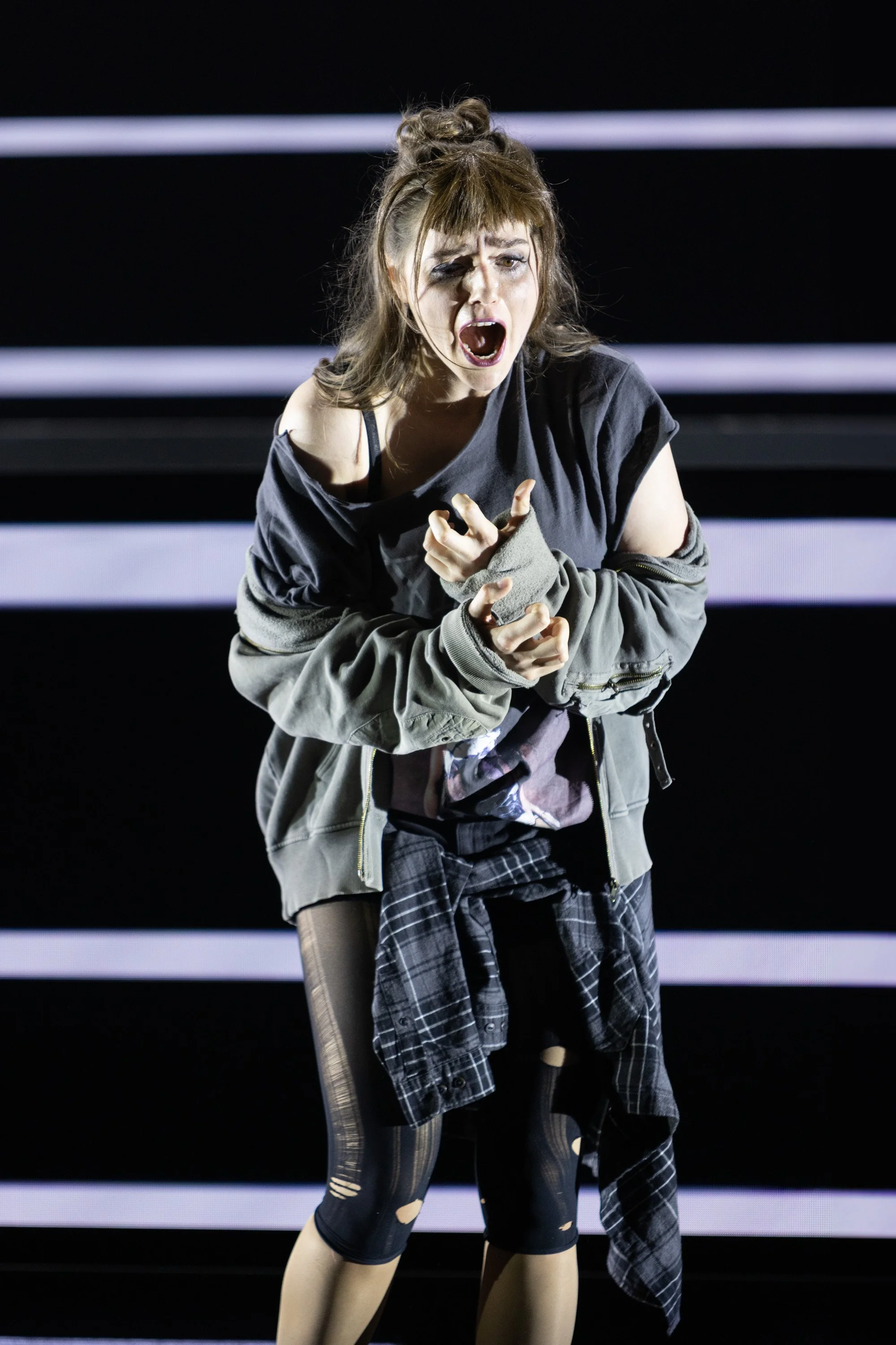 Eine Frau singt leidenschaftlich auf einer Bühne, mit dramatischem Gesichtsausdruck.