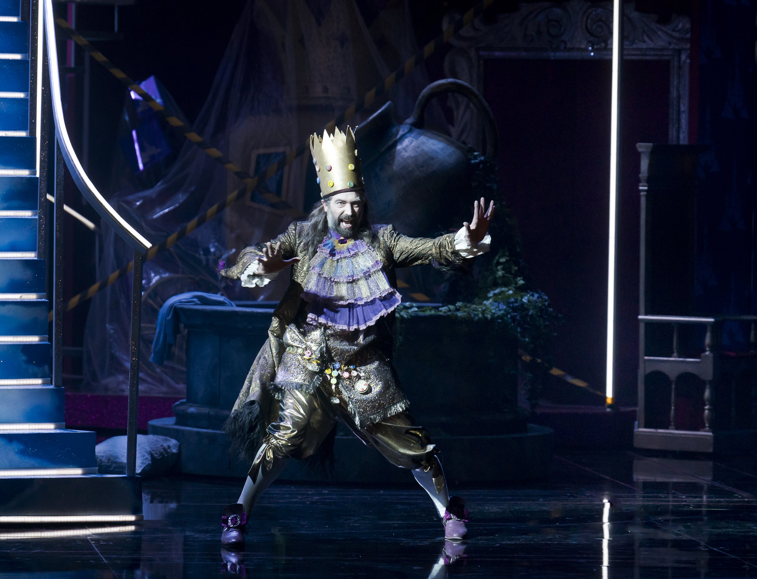 Männliche Person in einem königlichen Kostüm auf einer Bühne, die einen dramatischen Moment in einer Theaterproduktion darstellt.