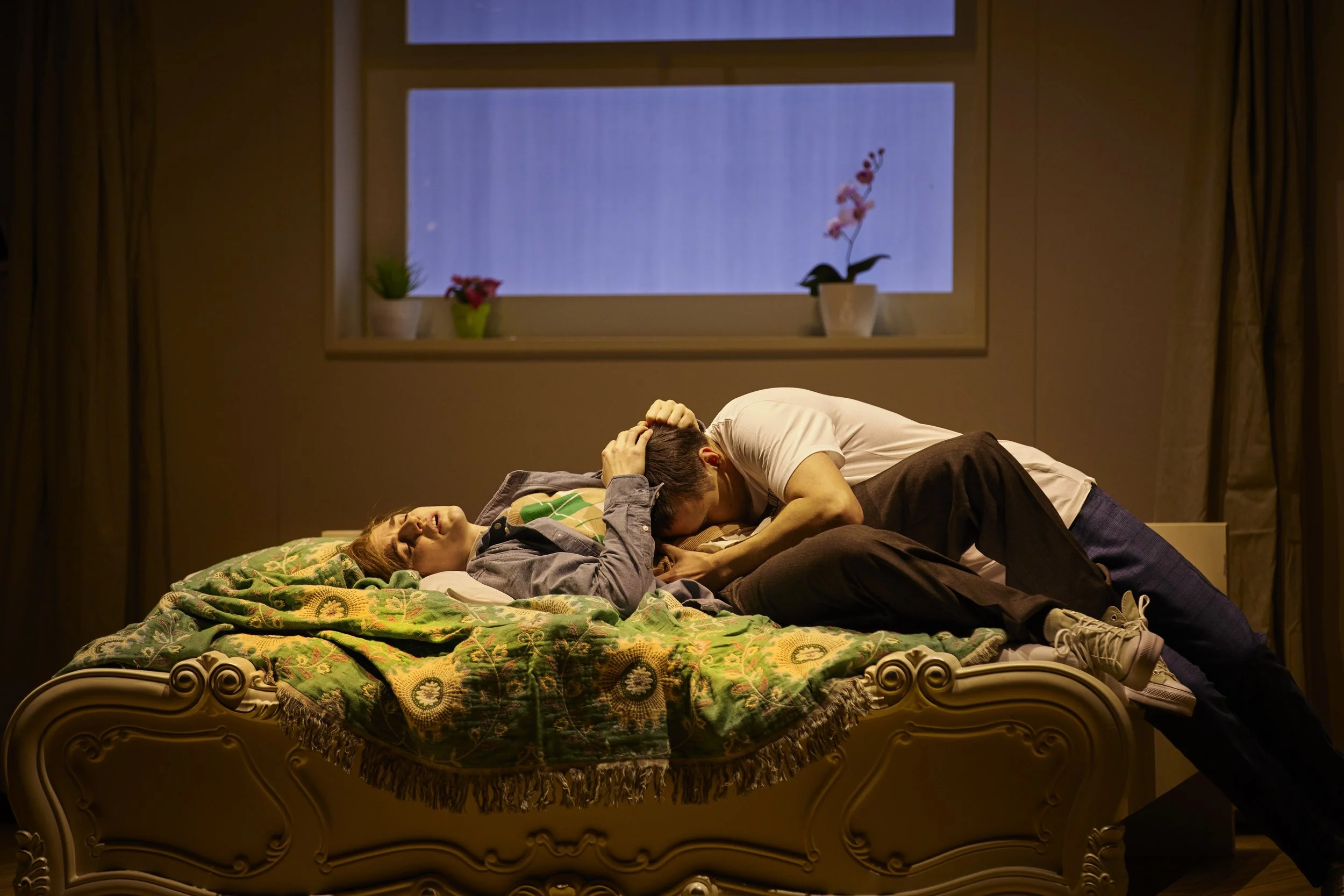 Ein Mann und eine Frau streiten im Bett, der Mann ist über die Frau gebeugt und greift ihren Kopf, die Frau schreit.