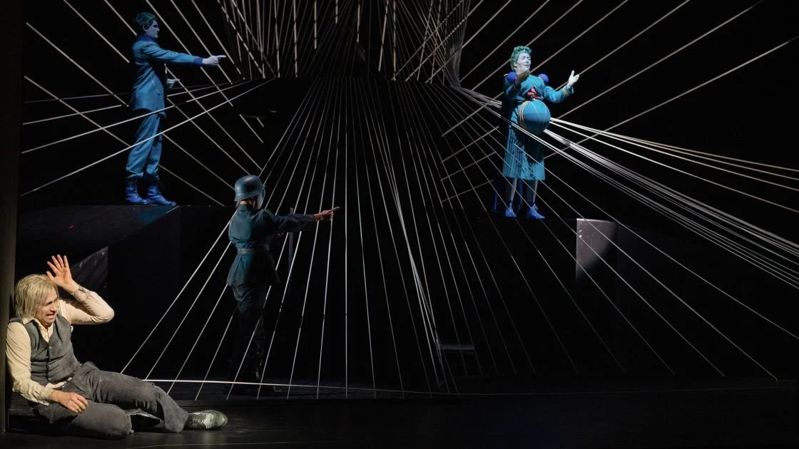 Theaterbühne mit vier Schauspielern in Kostümen und elektronische Kabel, die Texturen und Bewegungen darstellen.