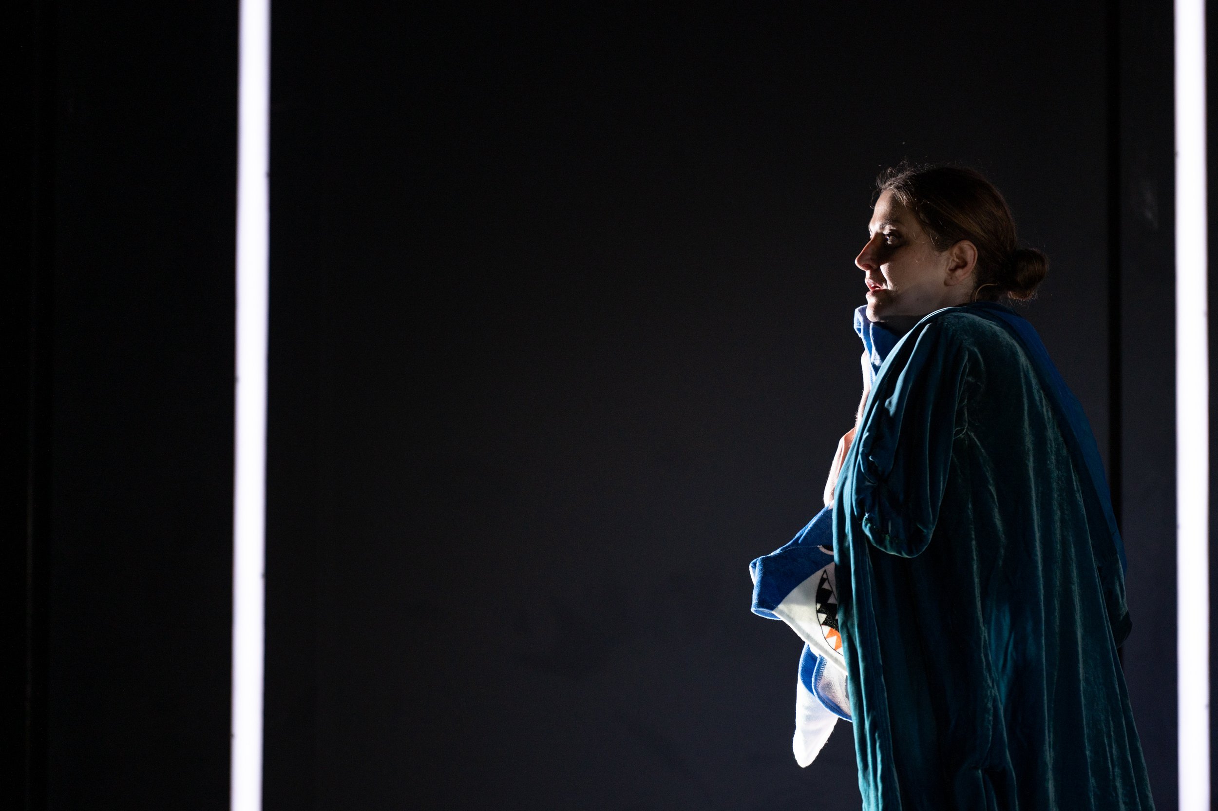 Frau im Trainingsanzug vor dunklem Hintergrund, die in Seitenansicht steht und ihren Kopf zur Seite dreht.