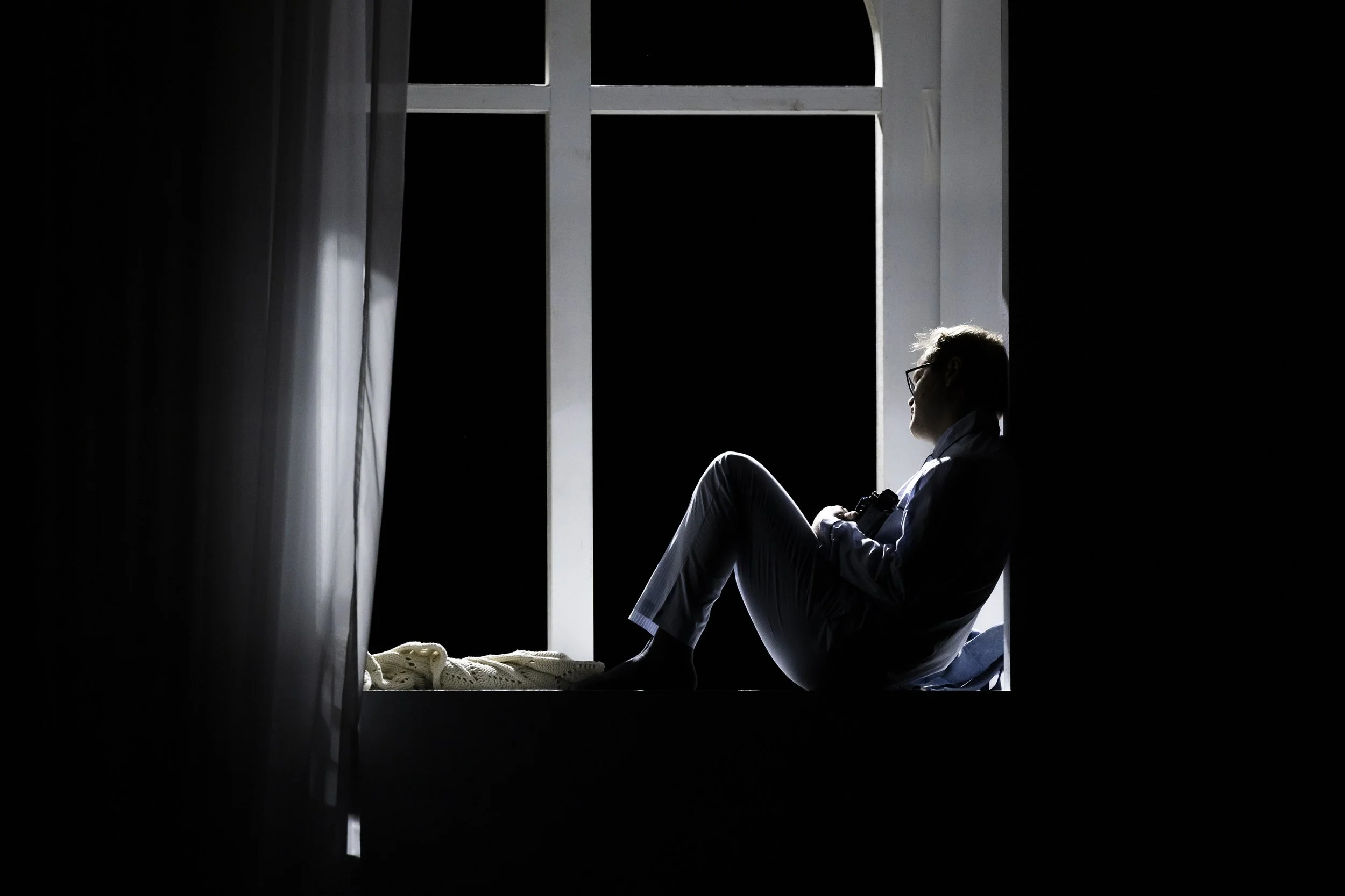 Silhouette einer Person sitzt auf einer Fensterbank bei Nacht, mit dunklem Himmel im Hintergrund, Sonnenlicht fällt auf die Person, die nach rechts blickt.