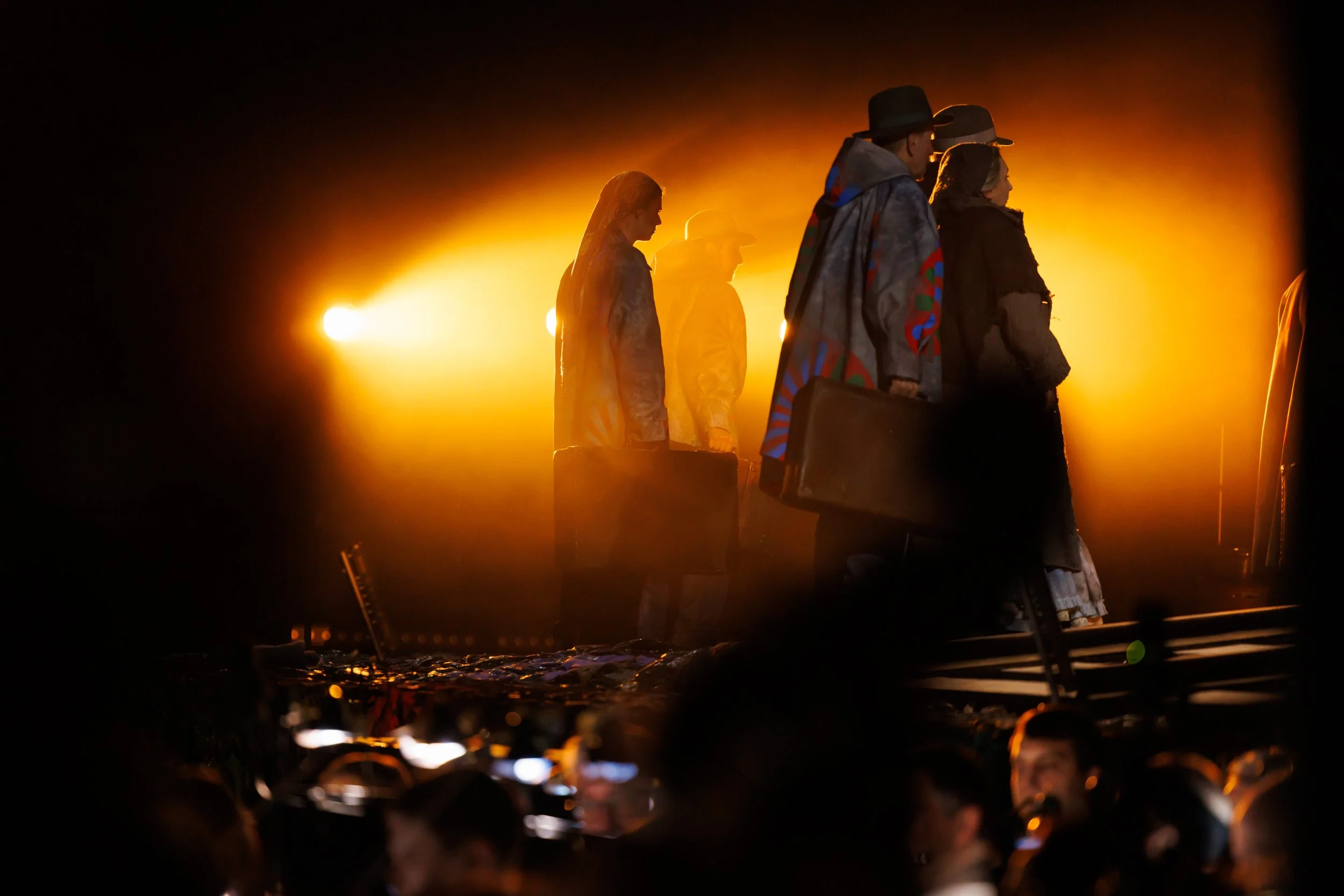 Menschen mit Koffern stehen auf einer Bühne bei rotem Licht in der Dunkelheit.