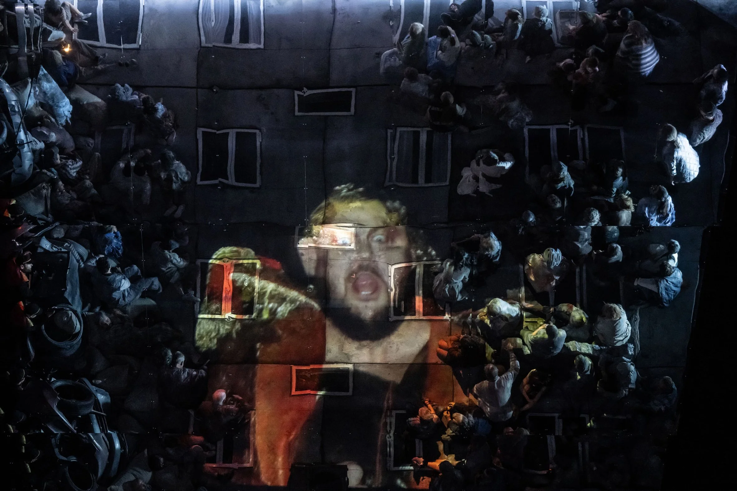 Große Menschenmenge schaut einen Filmprojektion an, auf der eine Frau zu sehen ist, vermutlich während einer Veranstaltung im Dunkeln.