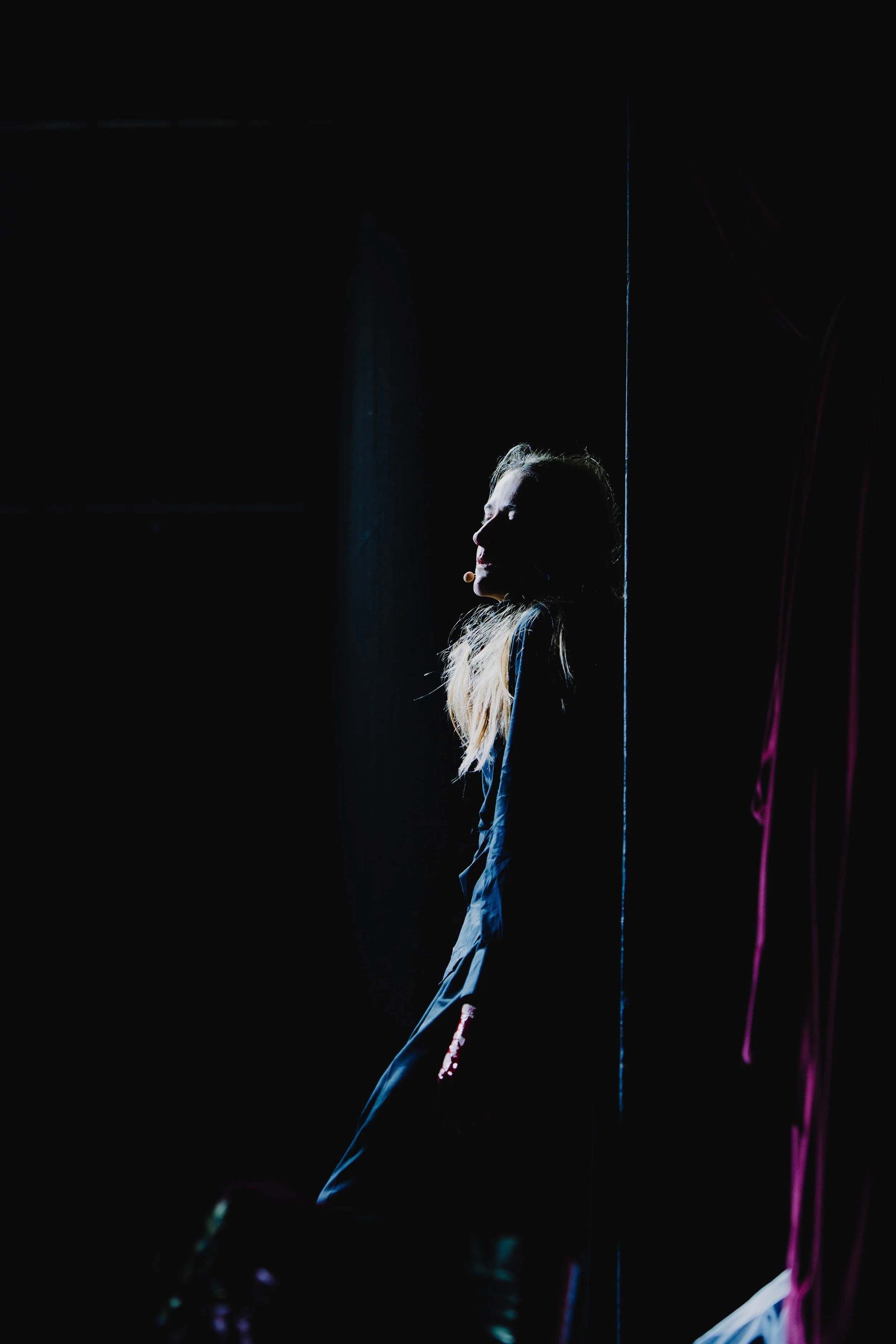 Frau steht im Schatten an einer dunklen Wand, nur ihr Gesicht und Haare sind schwach beleuchtet.