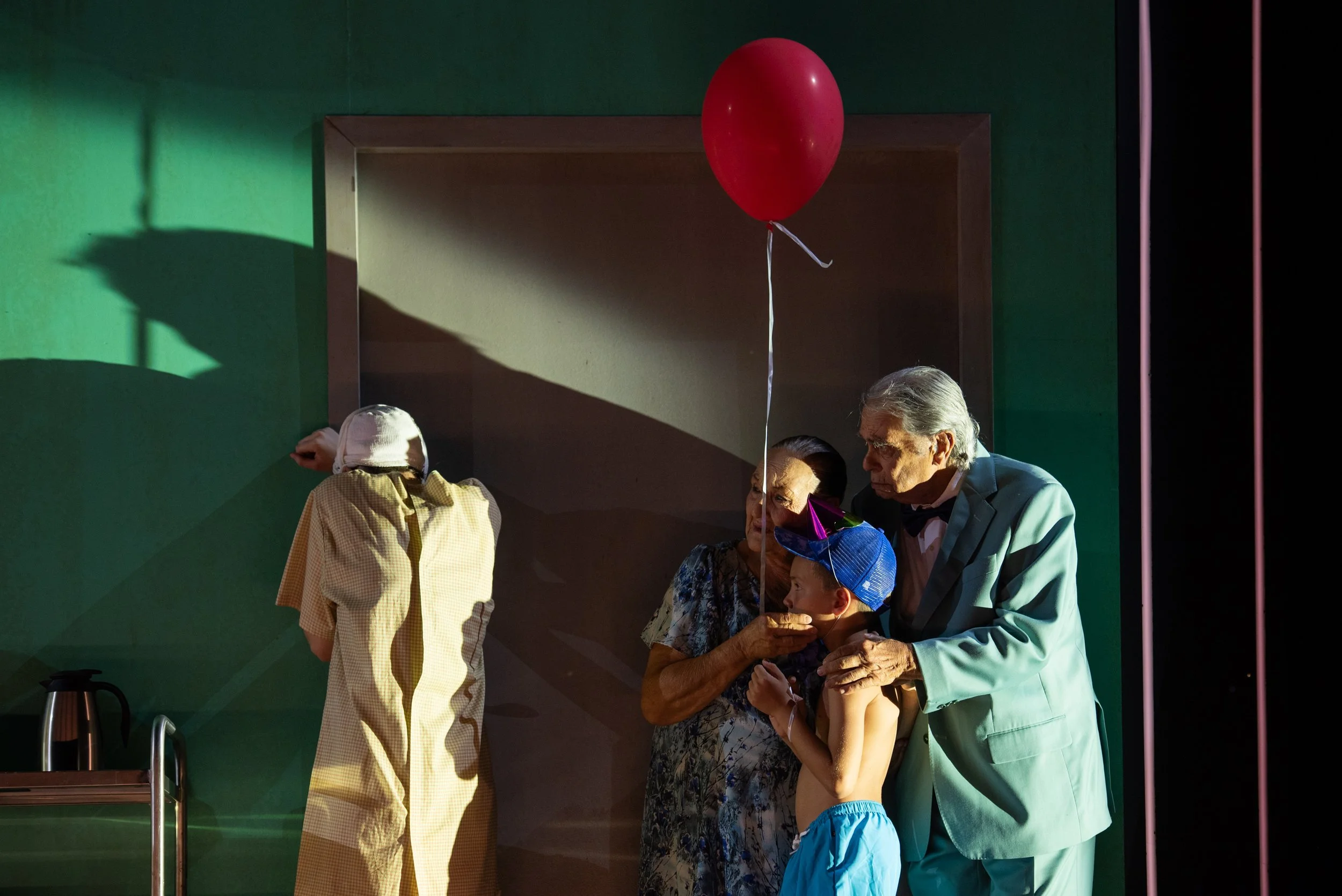 Ältere Menschen und ein Kind auf einer Bühne bei einer Theateraufführung, mit einem roten Ballon, der hoch oben schwebt.